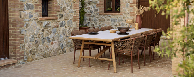 Una mesa de comedor de madera con sillas de mimbre elegantes, adornada con un tazón decorativo y una configuración de mesa minimalista.