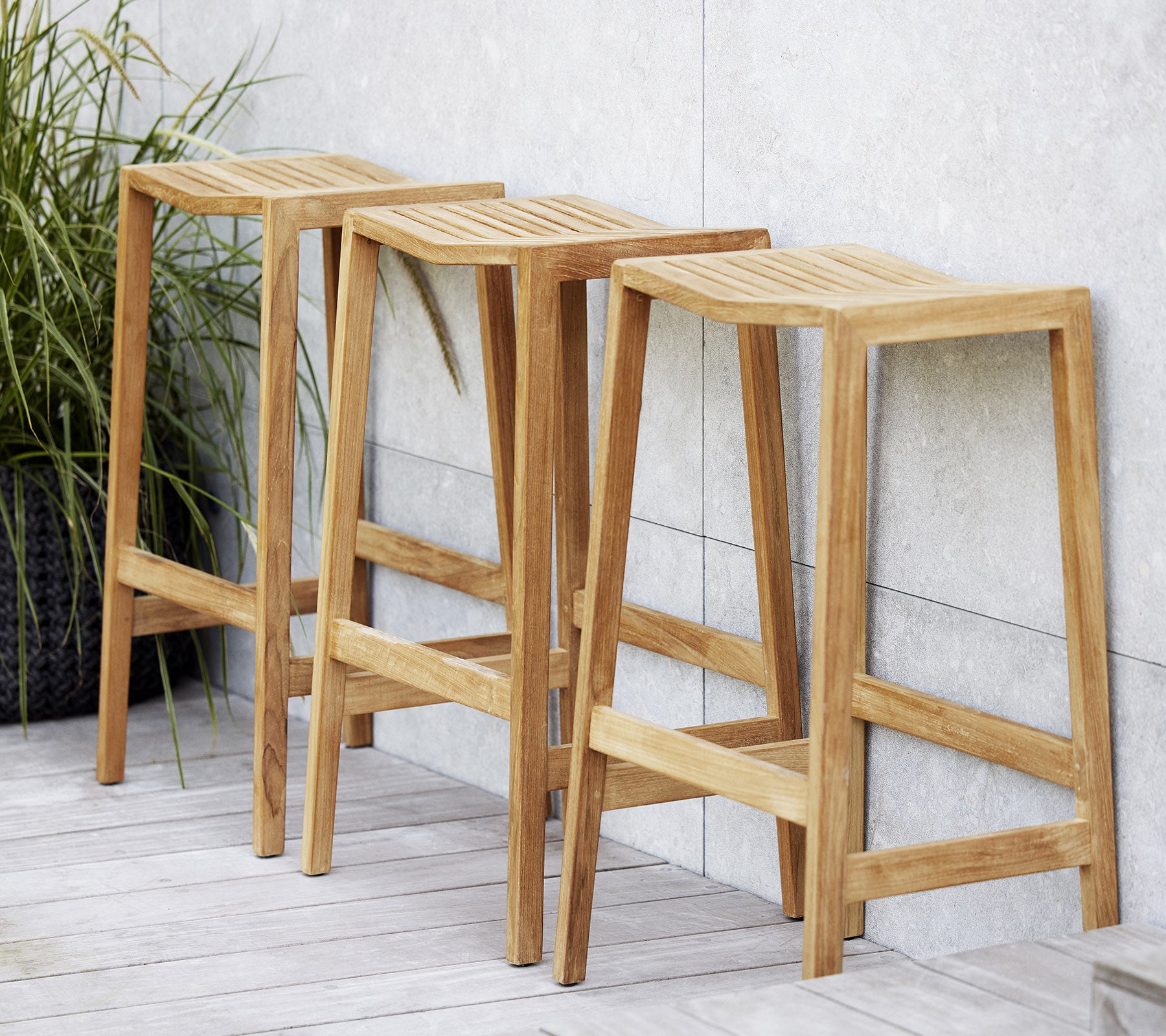Tres taburetes de bar de madera con asientos ranurados, con un diseño minimalista y líneas limpias, ubicados al lado de una planta decorativa.