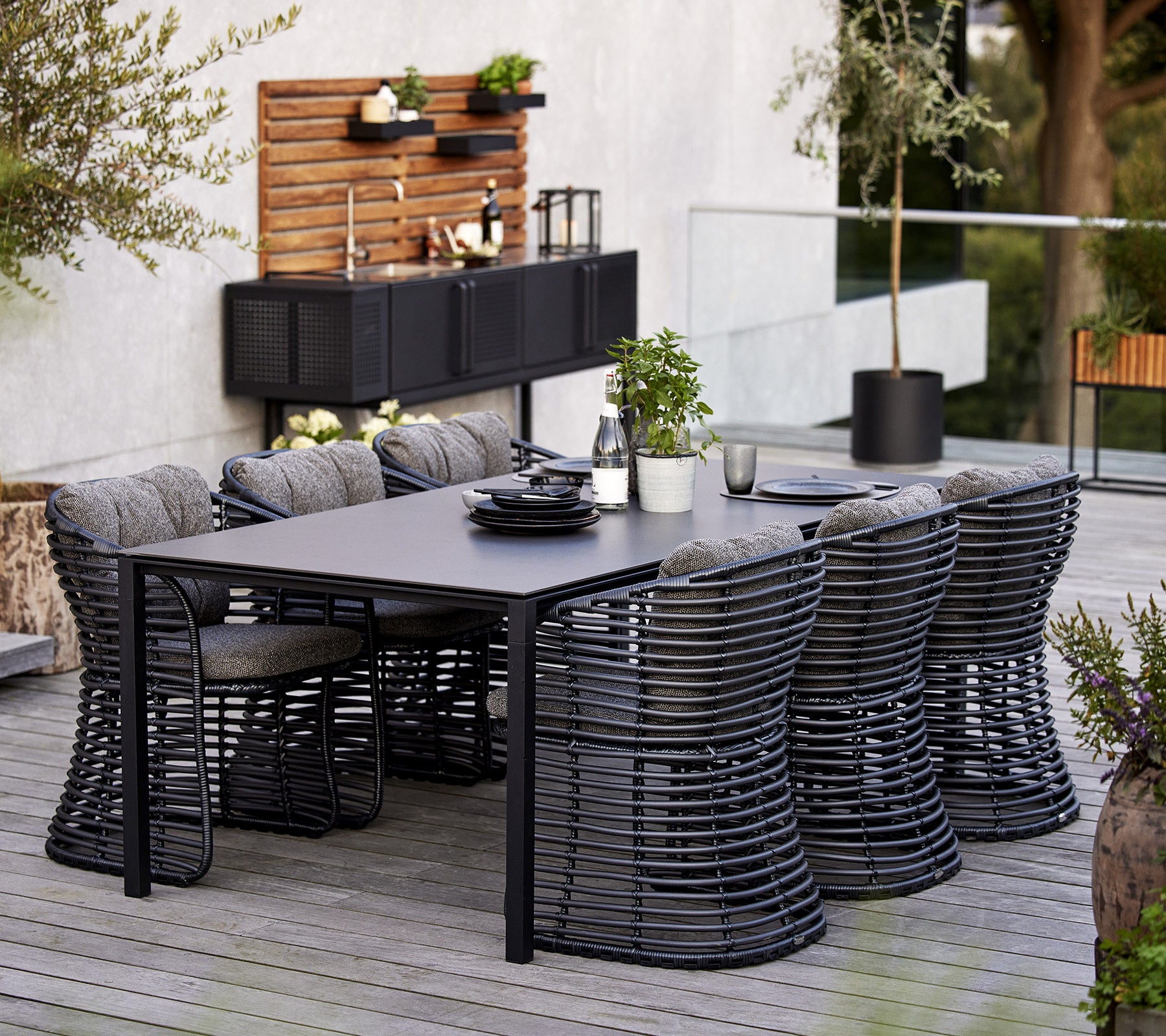 Un conjunto de comedor moderno que cuenta con una mesa rectangular y seis sillas de mimbre elegantes, complementado por elementos decorativos en el fondo.
