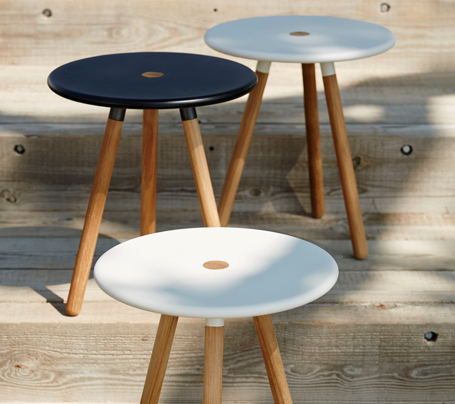 Tres taburetes minimalistas con tapas redondas en blanco y negro, cada uno sostenido por patas de madera, que exhiben un diseño moderno y elegante.