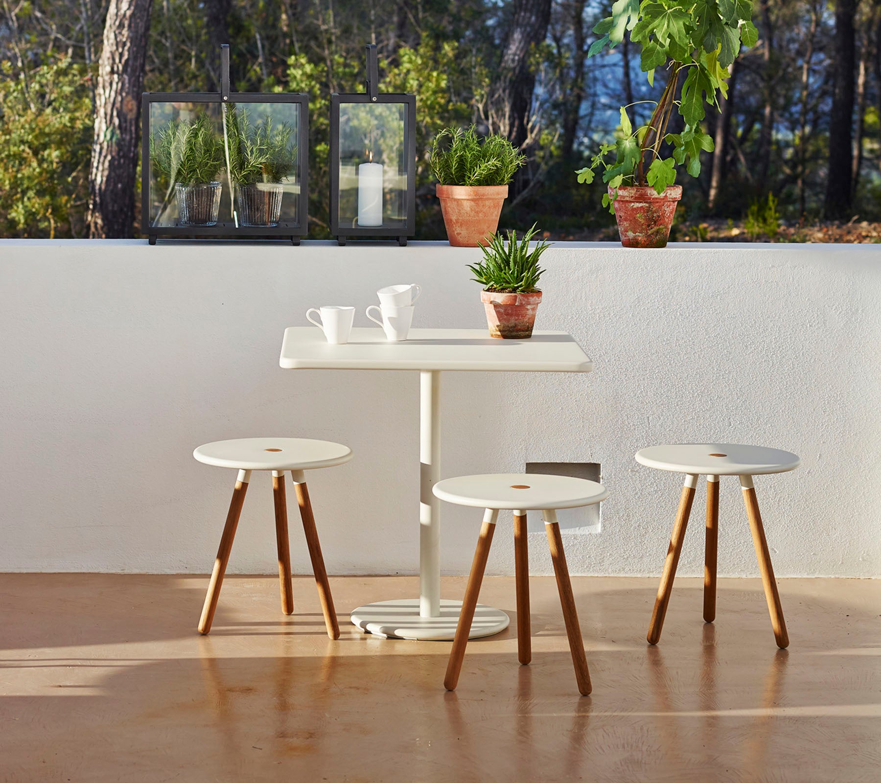 Una mesa minimalista con tres taburetes a juego, rodeada de plantas en macetas, creando una atmósfera serena y acogedora.