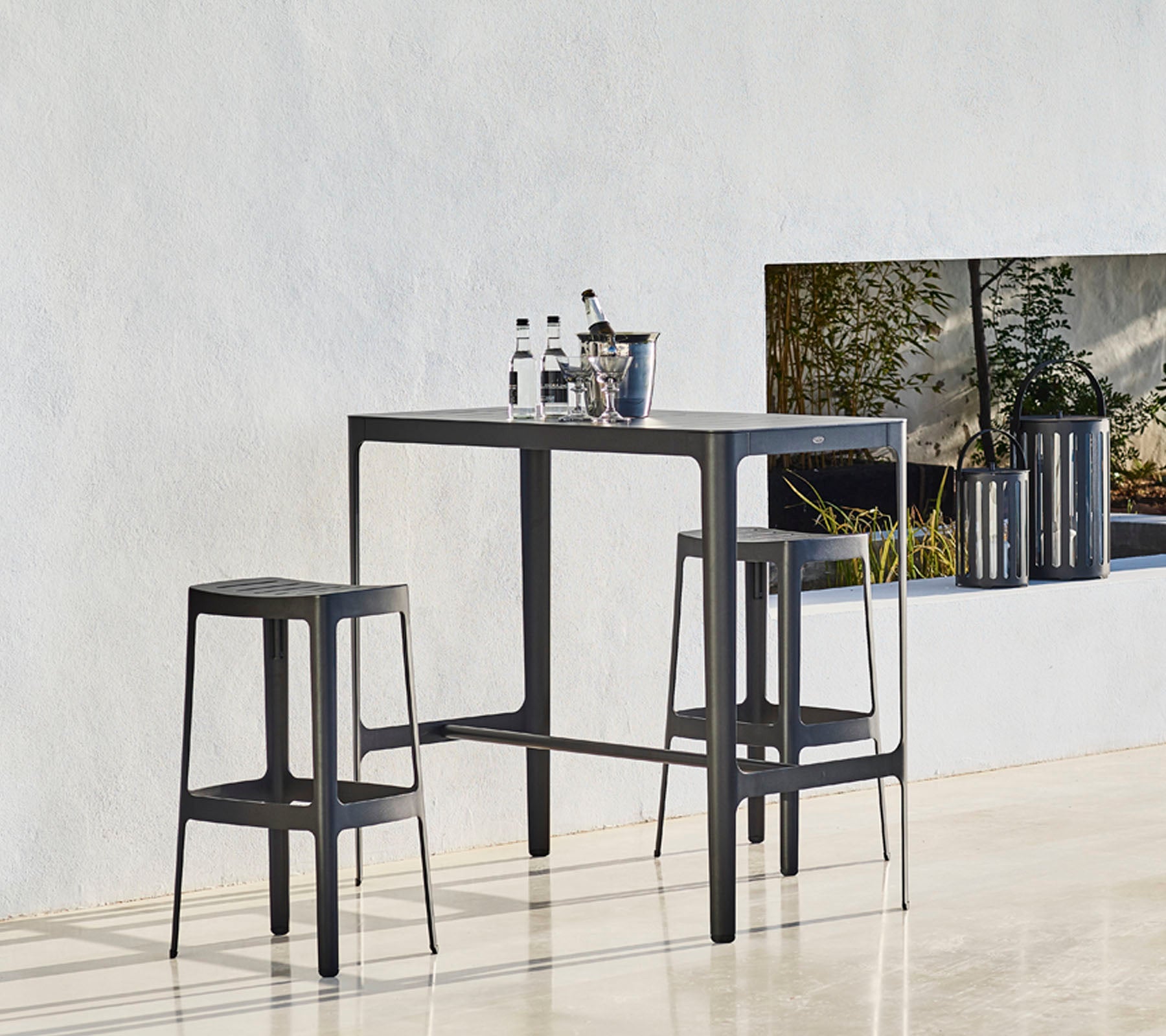 Una mesa elegante con dos taburetes a juego, con un diseño minimalista y botellas colocadas encima, contra un fondo neutro.