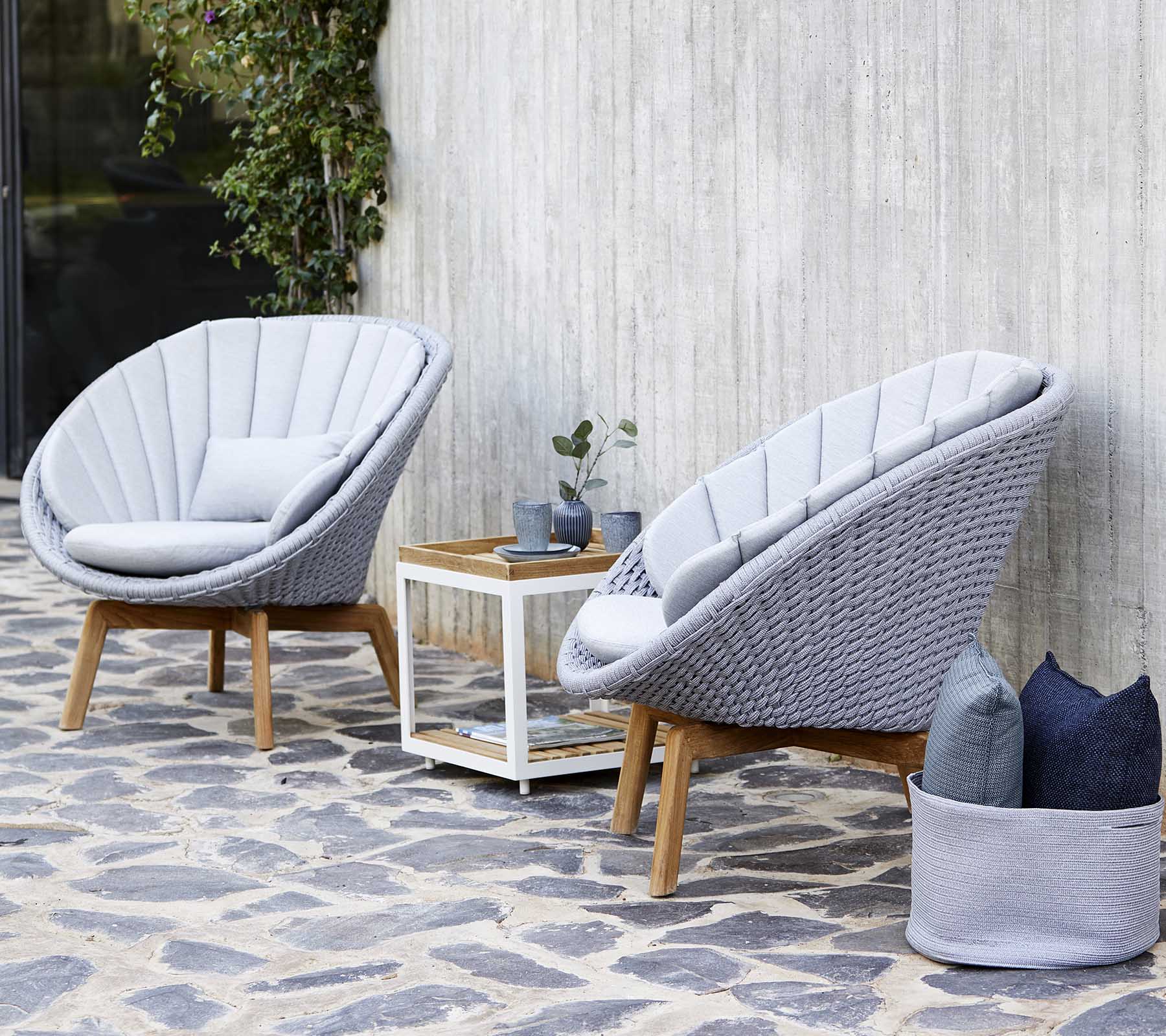 Dos elegantes sillones grises con un marco de madera están situados junto a una mesa auxiliar blanca, adornada con una pequeña planta y cojines decorativos.