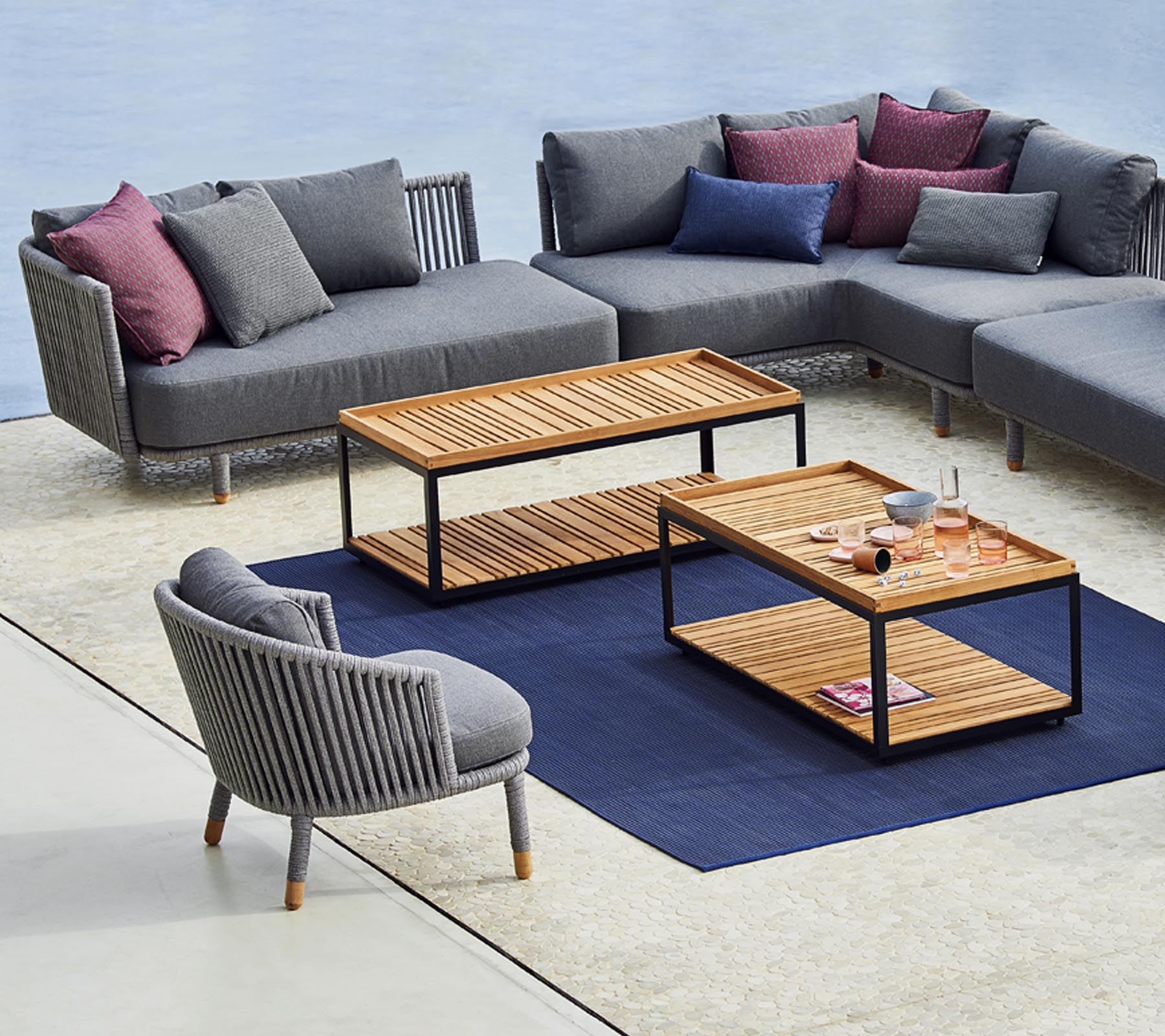 Distribución moderna de asientos con un sofá seccional gris, una silla redonda elegante y mesas de café de madera con una alfombra azul debajo.