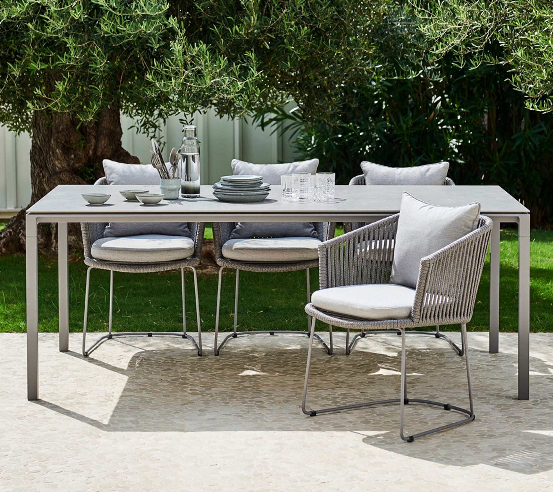 Un conjunto moderno de comedor al aire libre que cuenta con una mesa elegante, sillas acolchadas y una vajilla elegante dispuesta para una comida con estilo.