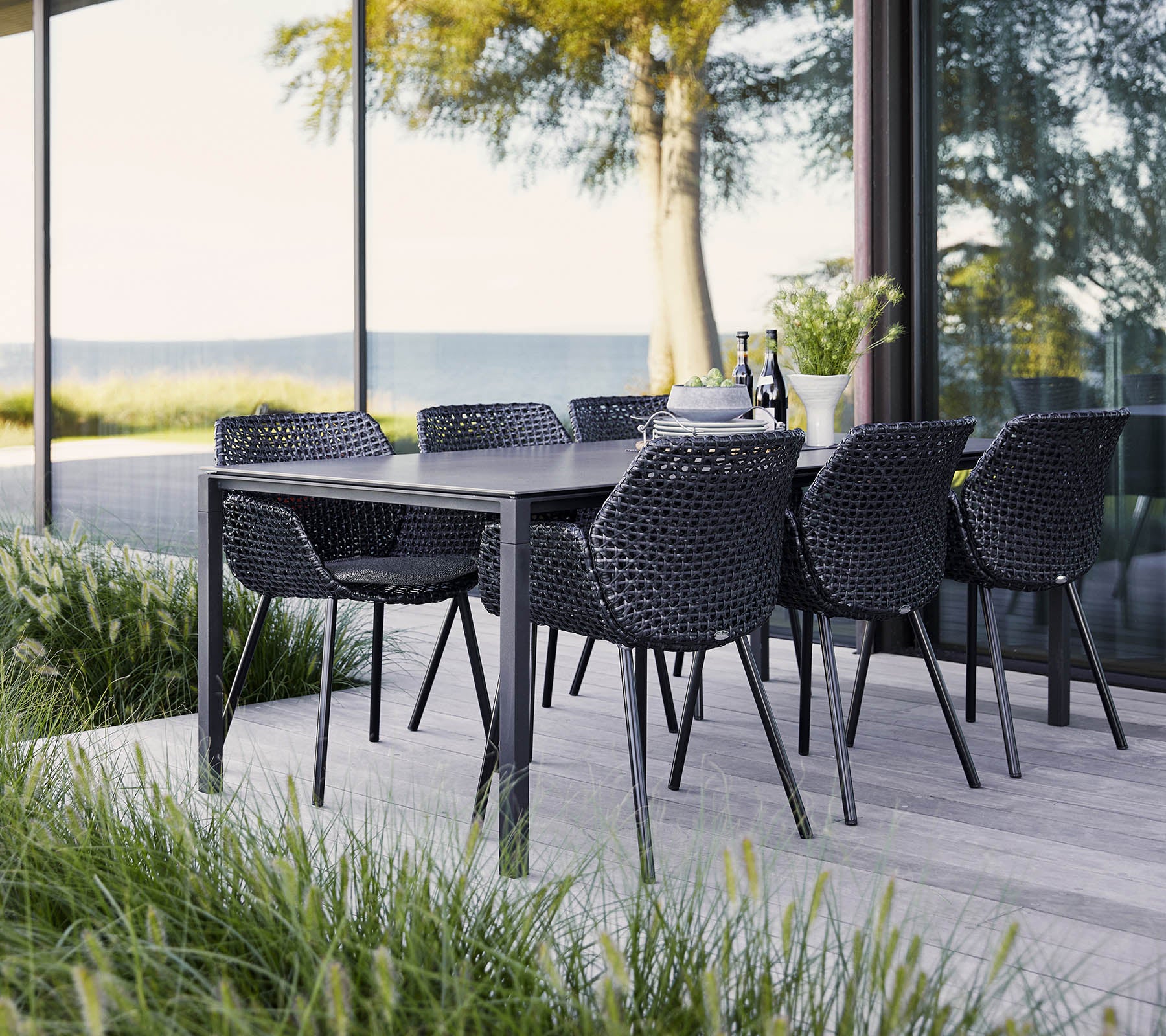 Un conjunto de comedor elegante con una mesa negra y sillas de mimbre, rodeado de vegetación exuberante y vistas expansivas. Ideal para reuniones.