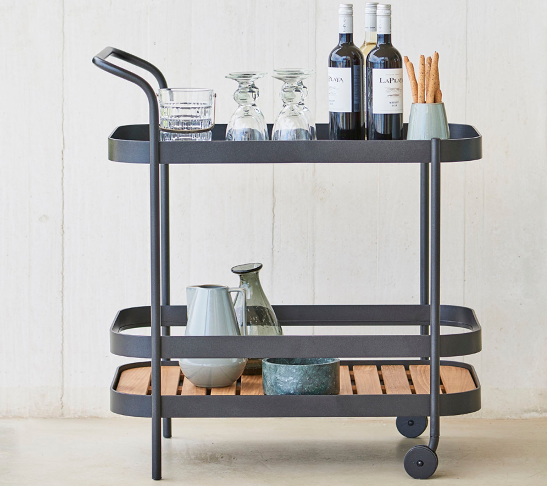 Un carrito de bebidas elegante con cristalería, botellas de vino y utensilios en tres niveles, con un marco de metal elegante y detalles de madera.