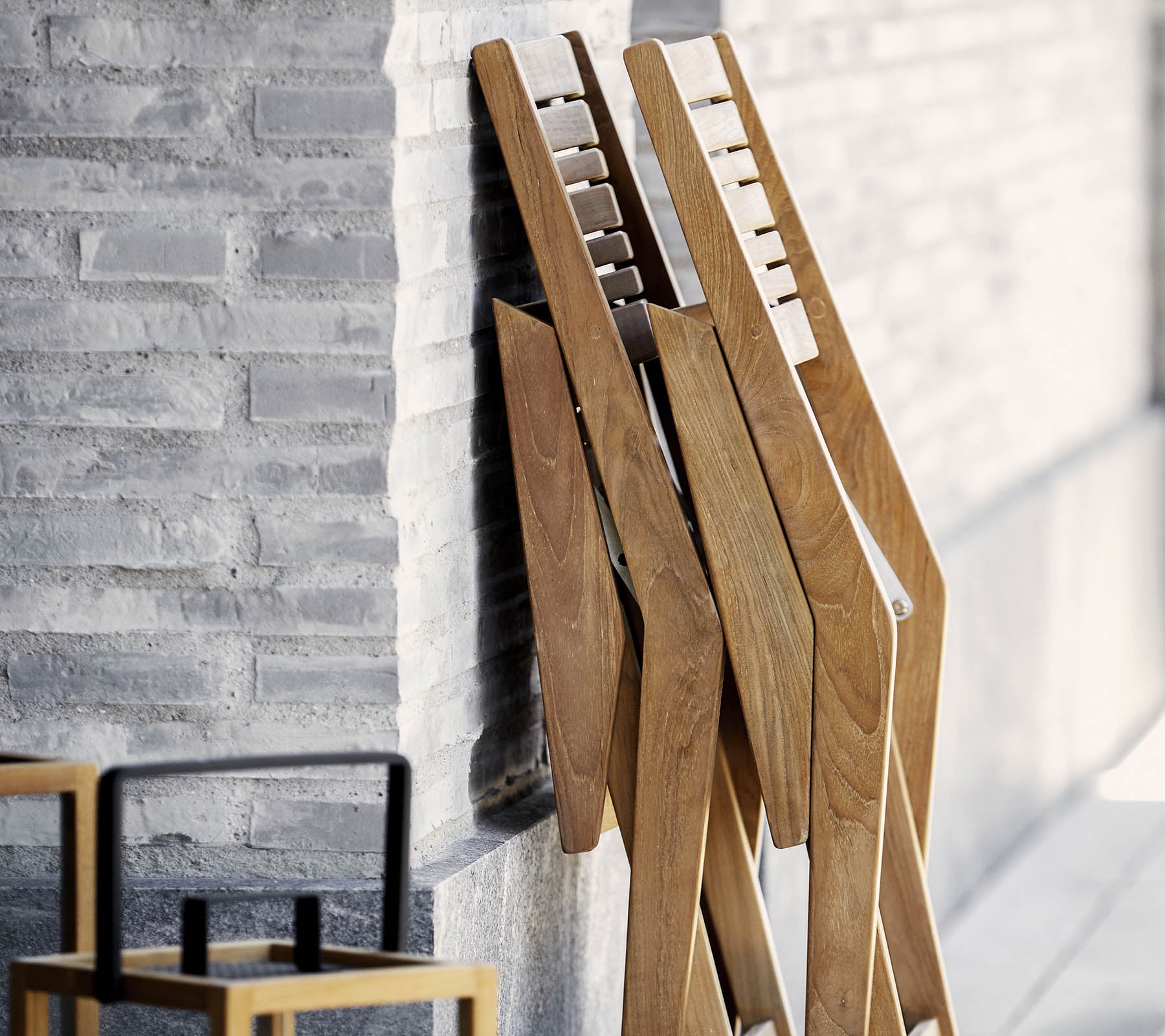 Tres soportes de madera de diseño elegante, apoyados contra una pared texturizada, acompañados de una silla sencilla y estilosa en primer plano.
