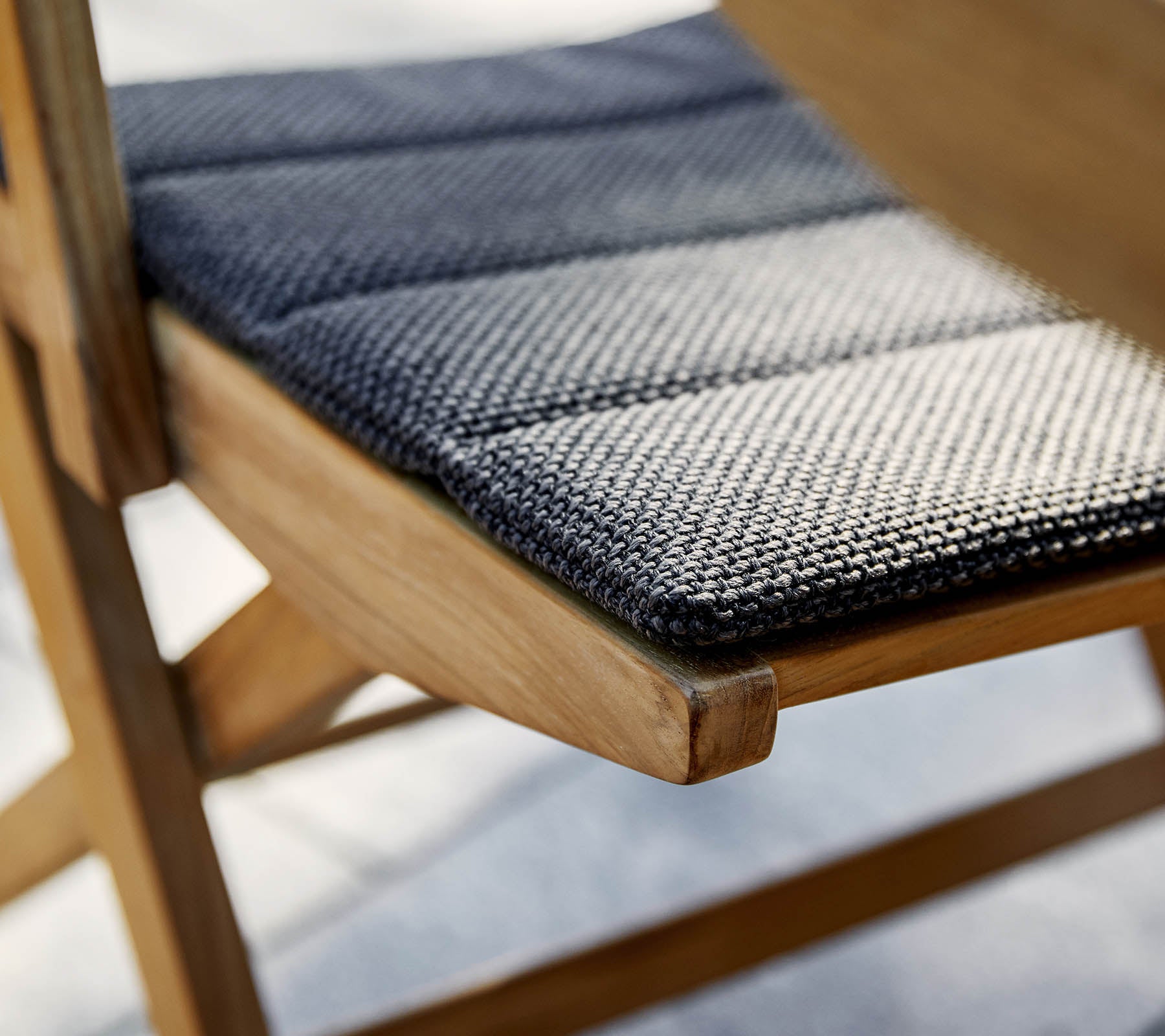 Primer plano de un asiento de silla con una tela texturizada en blanco y negro sobre un marco de madera, destacando la artesanía y los detalles.