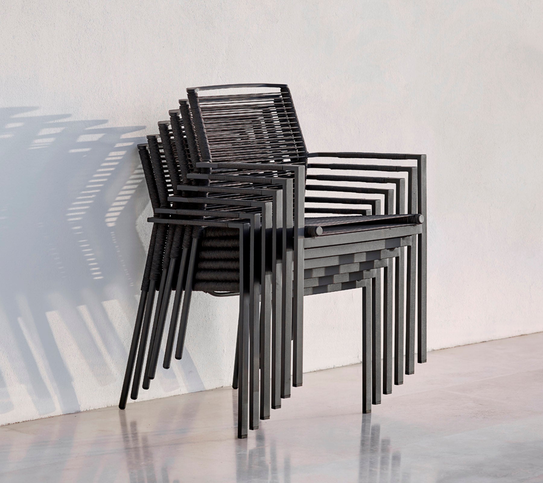 Una pila de sillas negras modernas con un diseño elegante, que proyecta sombras sobre un fondo claro.