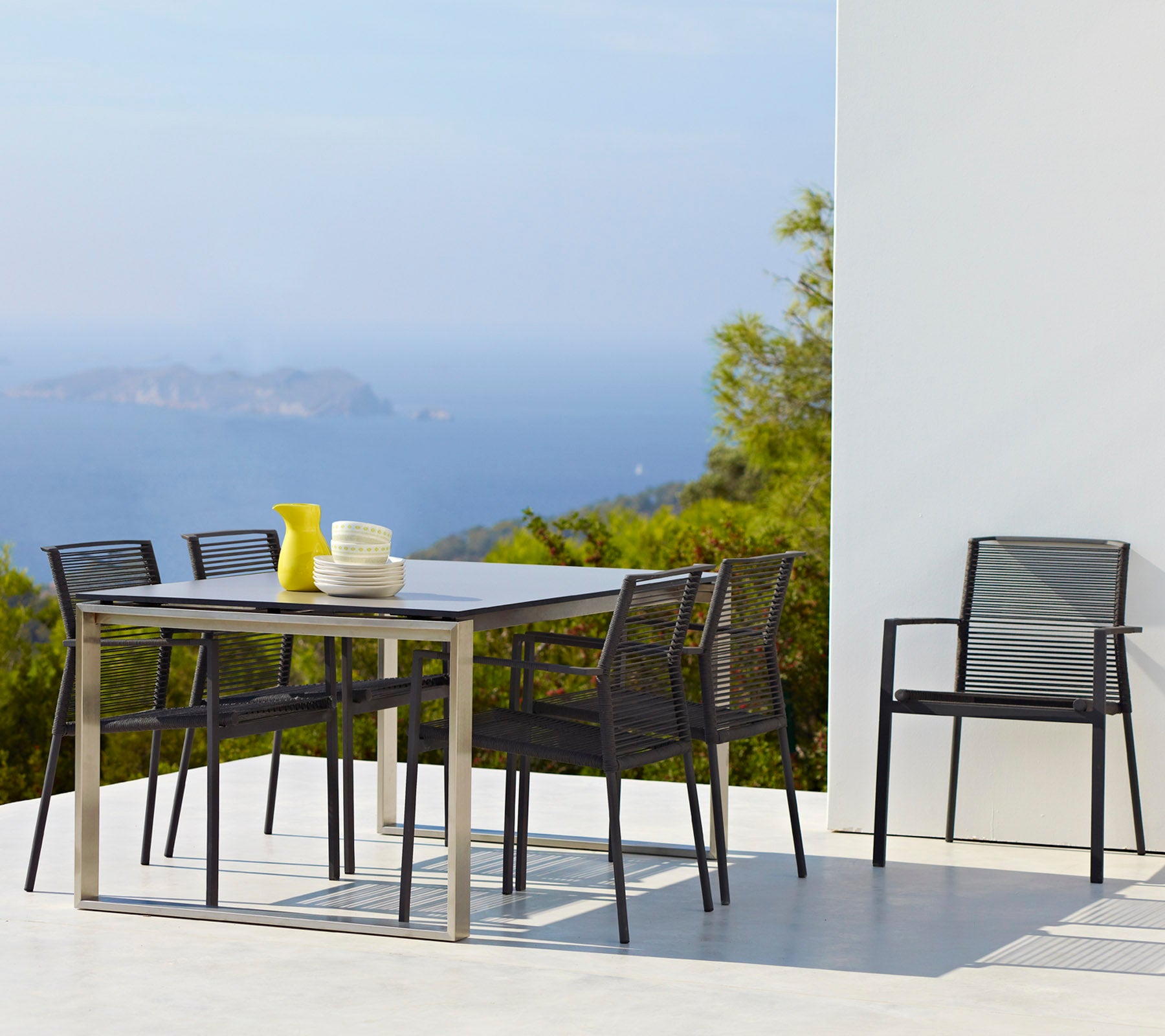 Un juego de comedor elegante que incluye una mesa rectangular, seis sillas y un jarrón con flores amarillas, situado contra un fondo escénico.