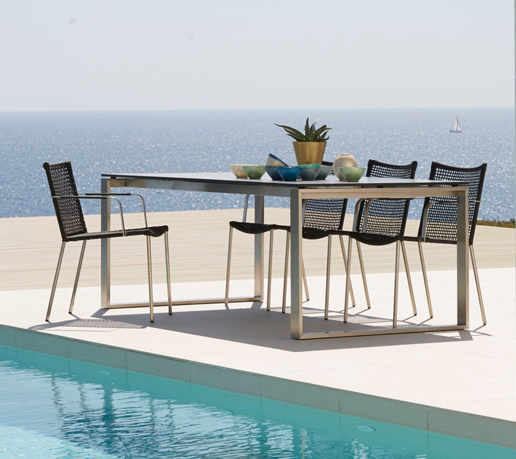 Una mesa de comedor moderna rodeada de elegantes sillas, adornada con objetos decorativos y con vistas a un mar tranquilo.
