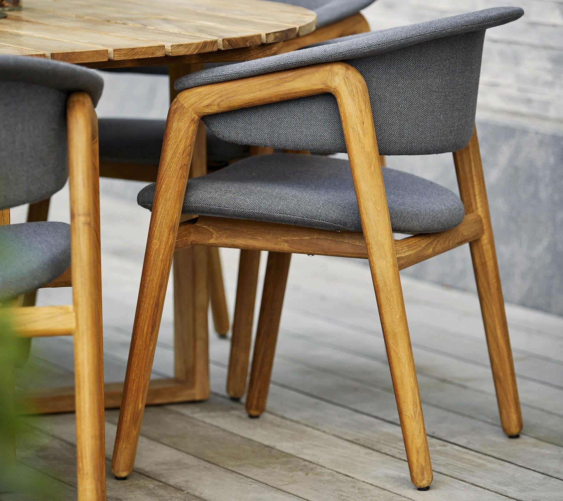 Silla de madera elegante con asiento y respaldo tapizados en gris, combinada con una mesa redonda de diseño contemporáneo.