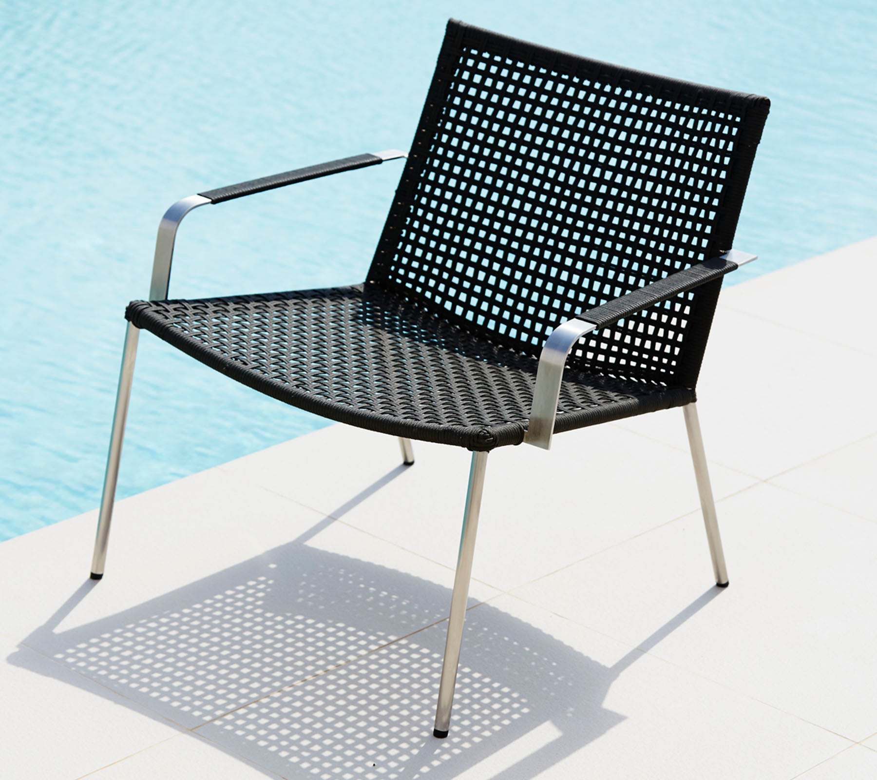 Silla negra elegante con un diseño perforado y patas de metal esculpidas, proyectando una sombra sobre una superficie clara.