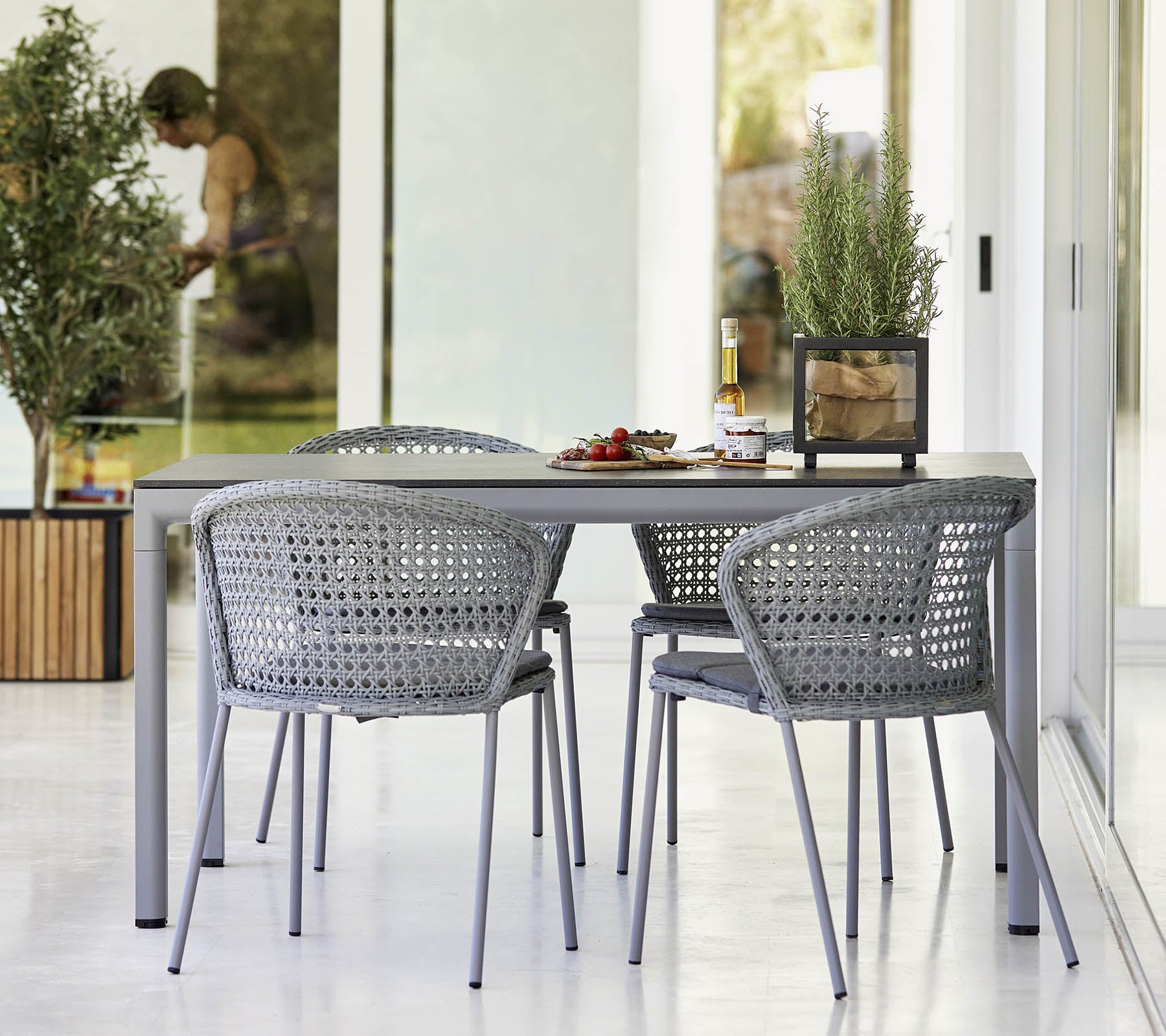 Juego de comedor moderno que presenta una mesa elegante y sillas trenzadas, complementado con vegetación y una atmósfera ligera y aireada.