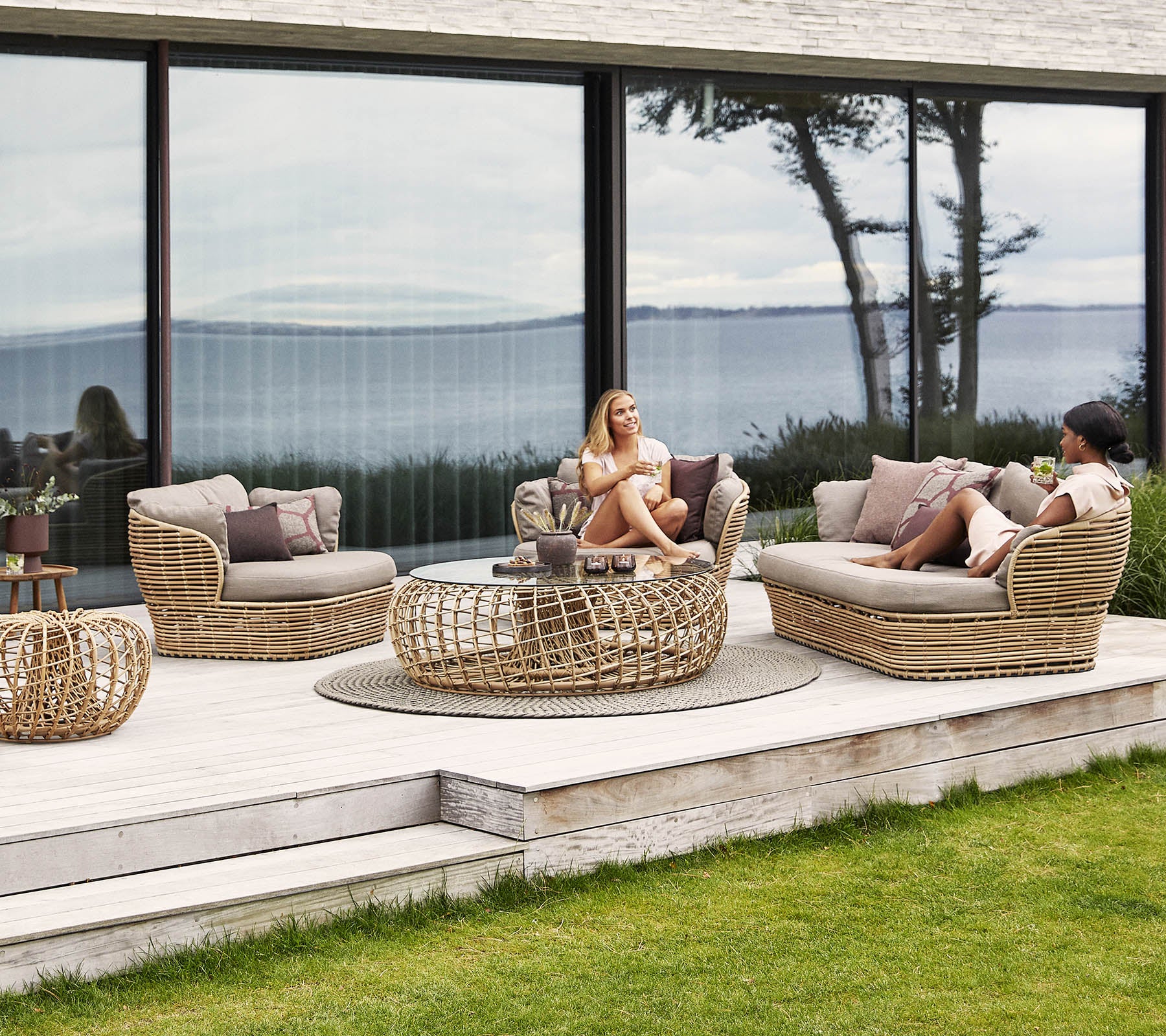 Una área de estar de mimbre elegante con cojines, que cuenta con una mesa de café y vistas serenas en el fondo, ideal para la relajación.