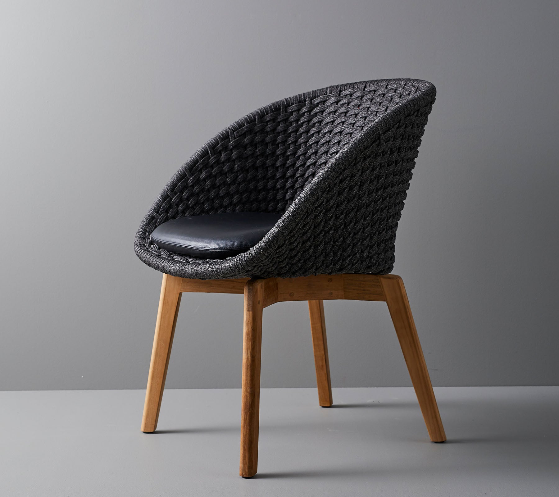 Silla tejida elegante con un cojín cómodo, con patas de madera suaves y cónicas y un diseño moderno adecuado para diversos entornos.