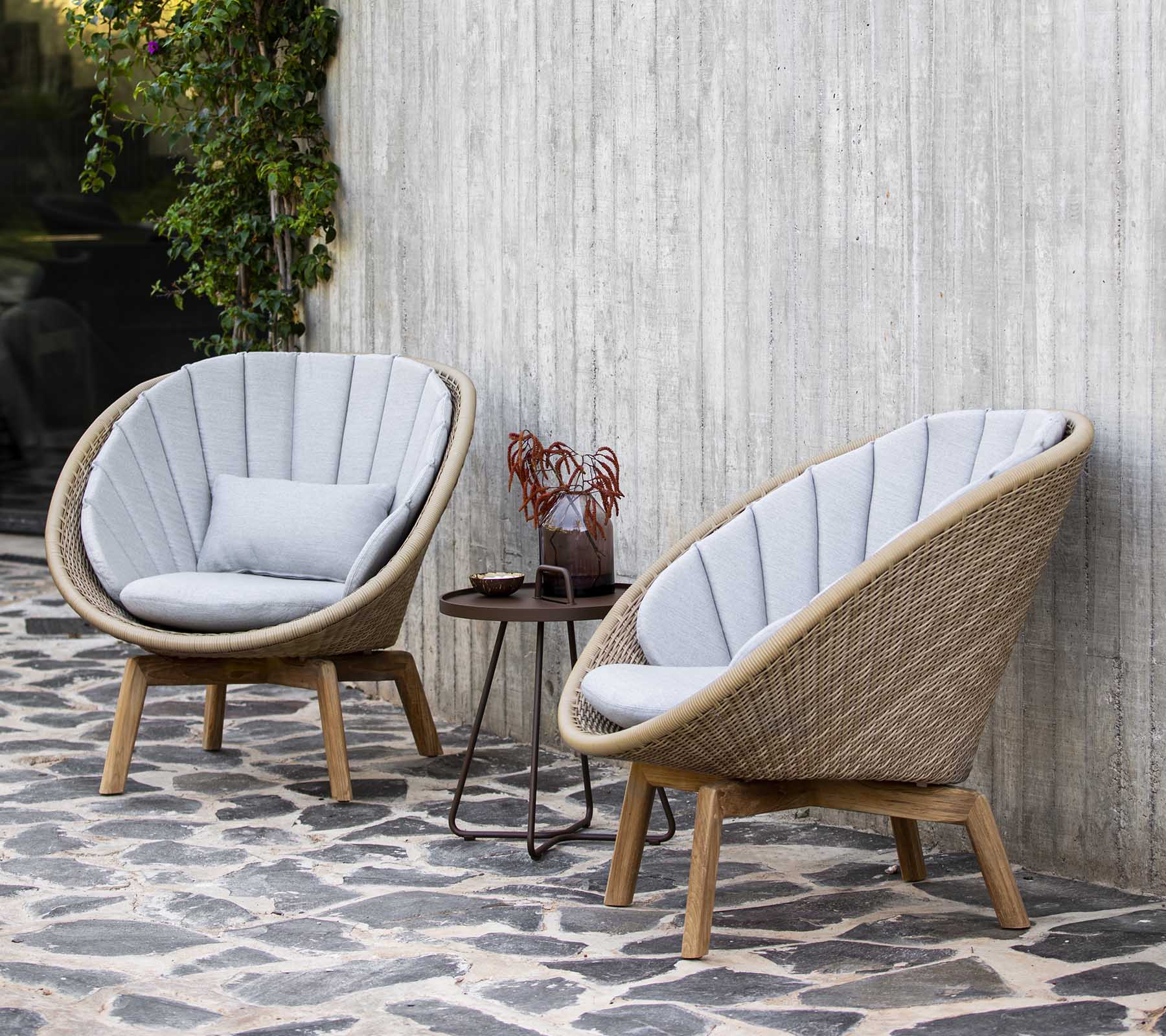 Dos sillones elegantes y curvados con suaves cojines grises al lado de una pequeña mesa adornada con elementos decorativos, situada contra una pared texturizada.