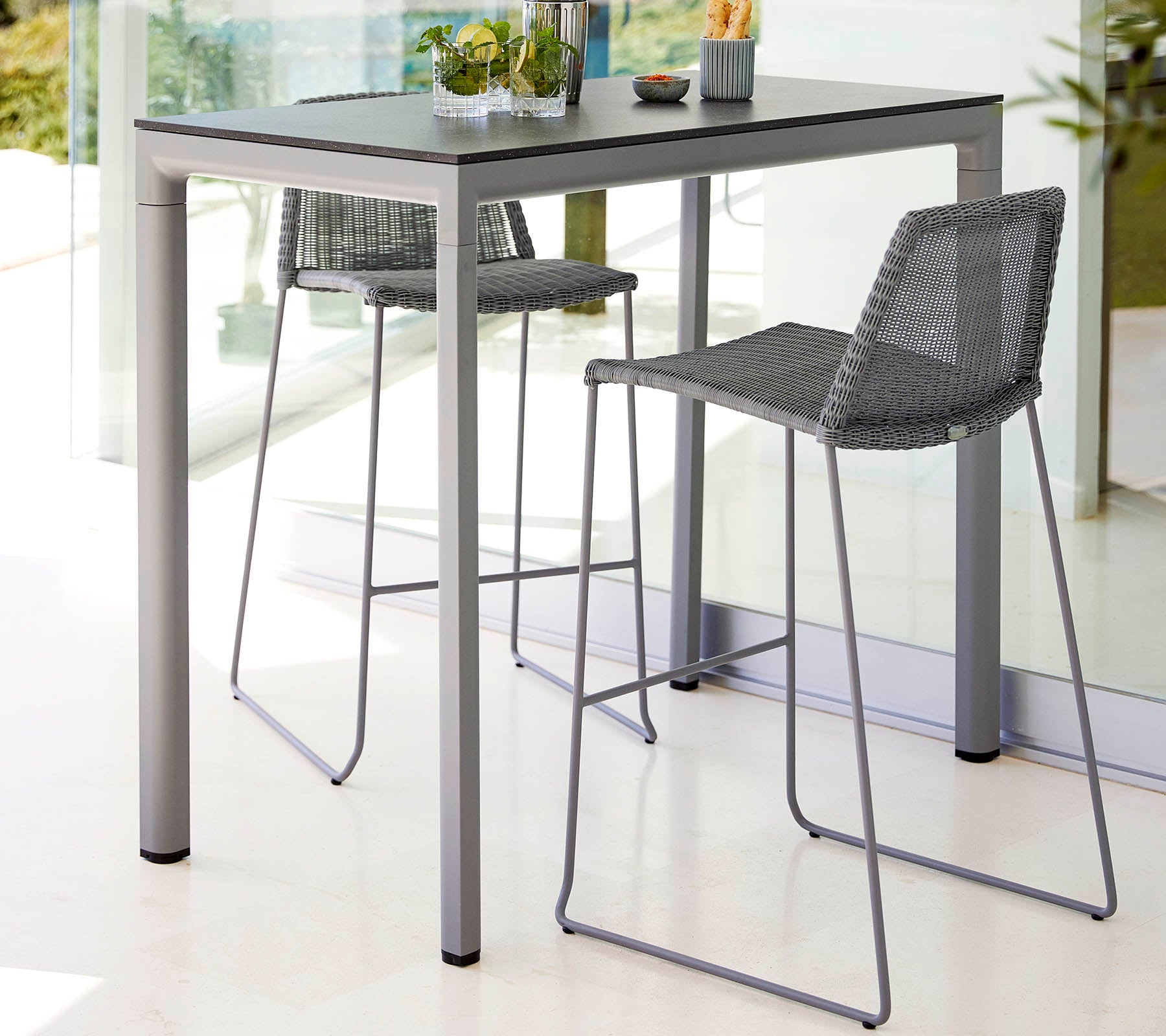 Una mesa elegante con dos taburetes altos, que presenta un diseño moderno y una paleta de colores claros, complementada con una pequeña planta como centro.