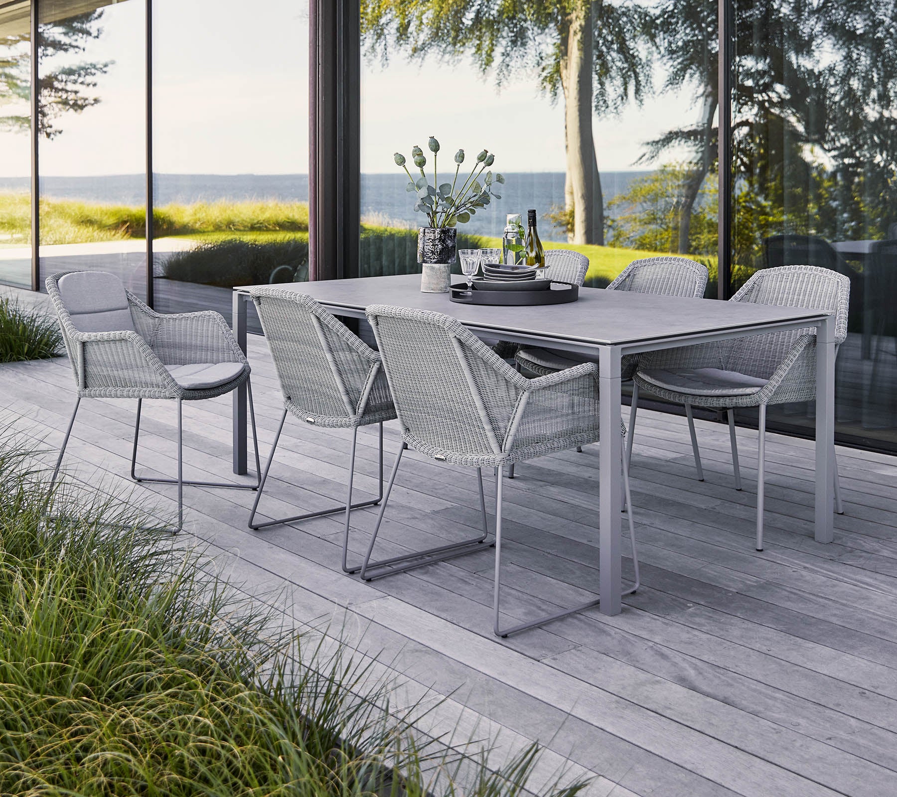 Un conjunto de comedor al aire libre elegante que cuenta con una mesa rectangular y seis sillas trenzadas, rodeado de vegetación y una vista escénica.