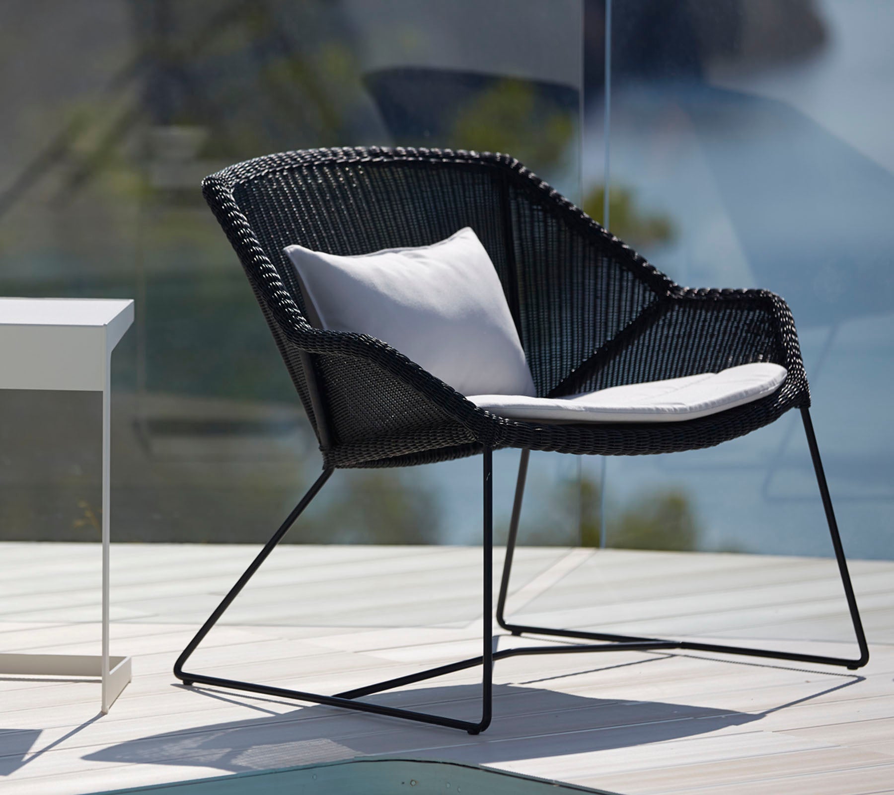 Silla negra moderna con cojín blanco en un elegante entorno de salón al aire libre.