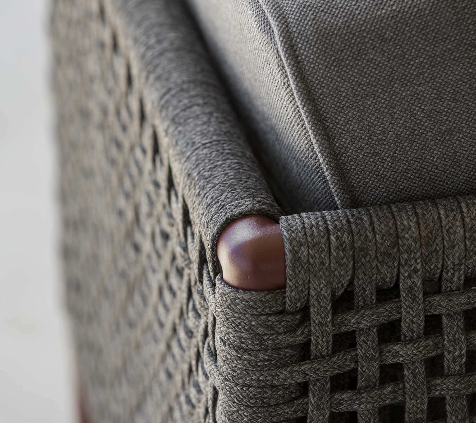Primer plano de una esquina de mueble tejido con elegante tela gris y suaves acentos de madera, que muestra una mezcla de textura y estilo.