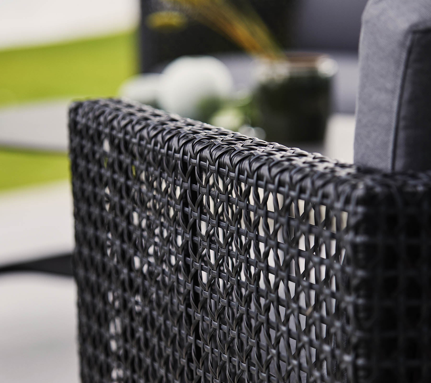 Respaldo de silla negro tejido con un cojín suave, con elementos decorativos borrosos en el fondo.