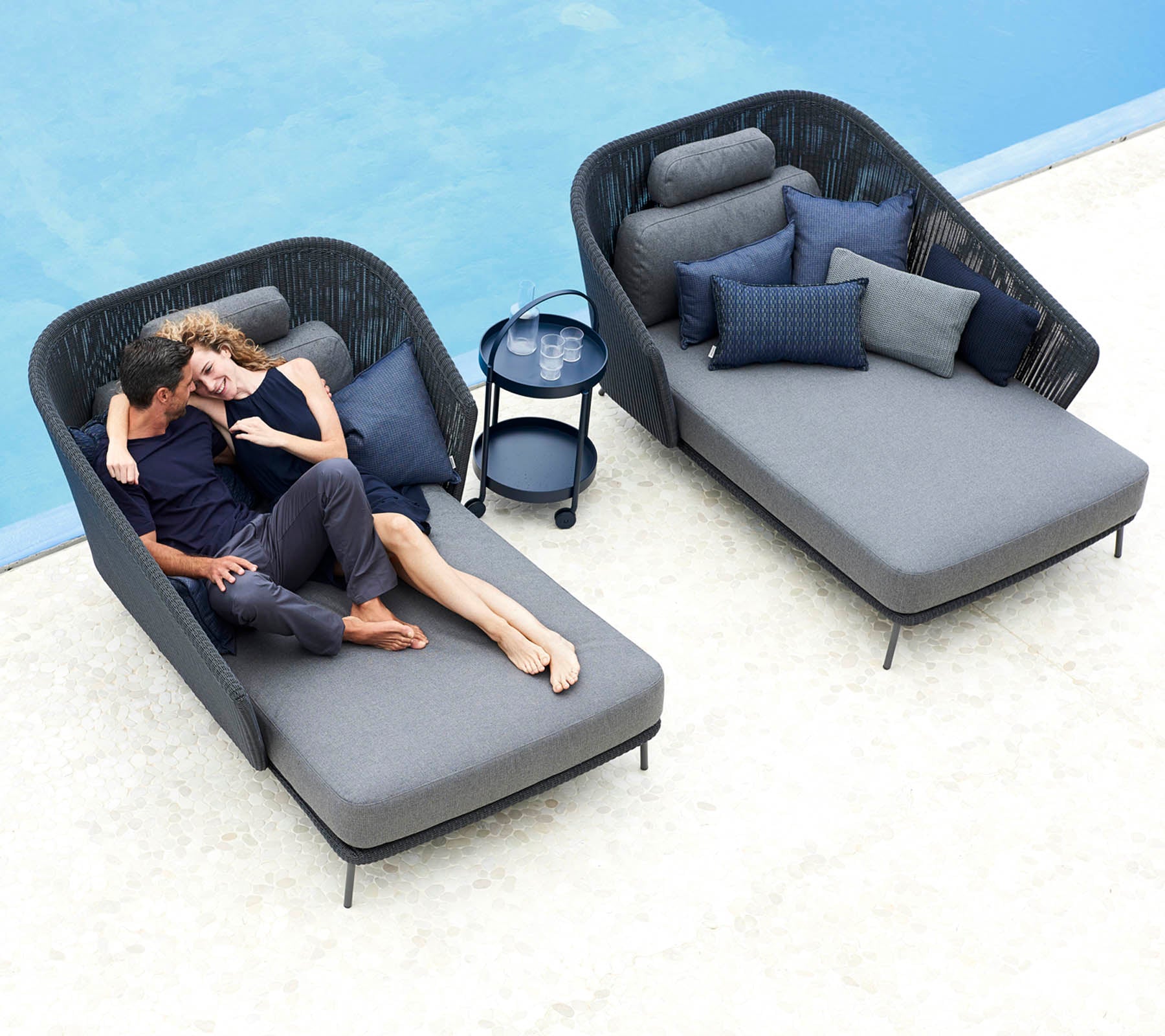 Una pareja se relaja junta en sillas de lounge elegantes con cojines suaves, acompañada de una pequeña mesa auxiliar y cojines decorativos.