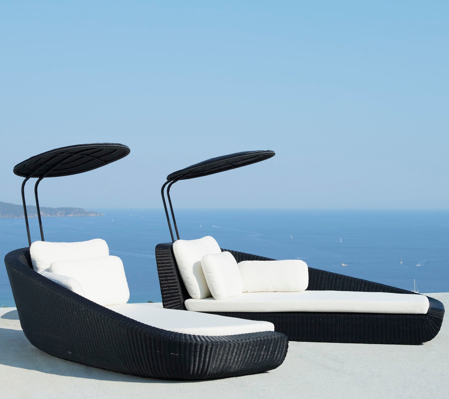 Dos sillas de lounge elegantes con cojines blancos y toldos curvados, con un hermoso fondo de océano azul.
