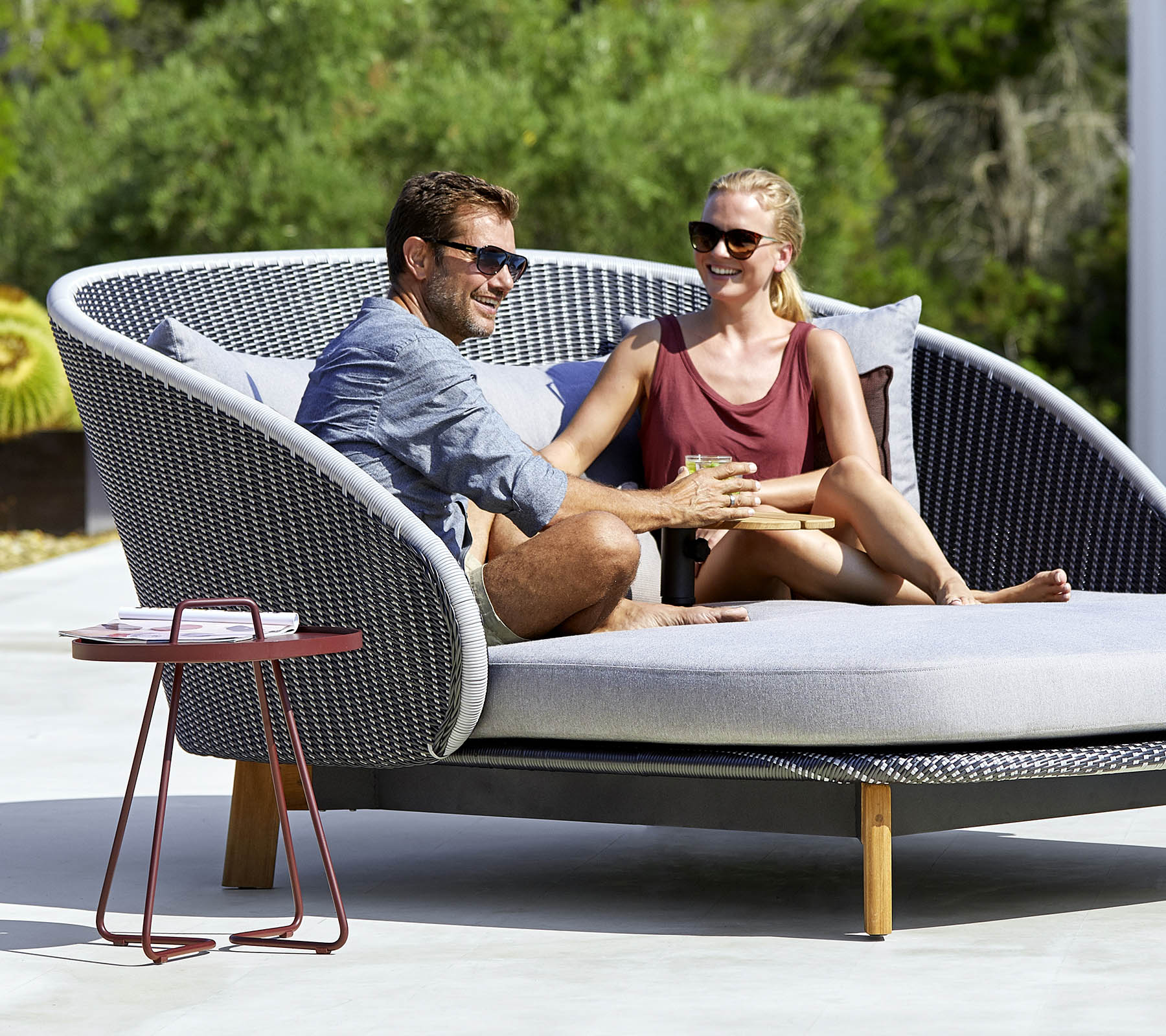 Una pareja disfruta de un momento acogedor juntos en un sofá de exterior elegante y curvado con una mesa auxiliar cerca.