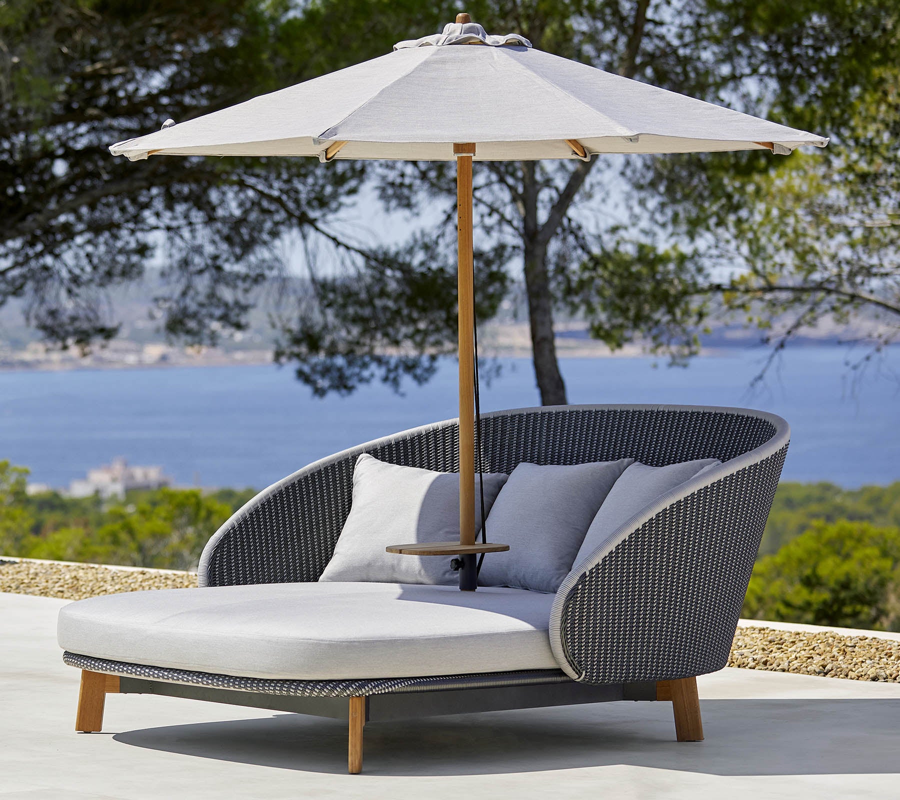 Silla de lounge exterior elegante con cómodos cojines y una gran sombrilla para sombra, ubicada contra un fondo escénico.