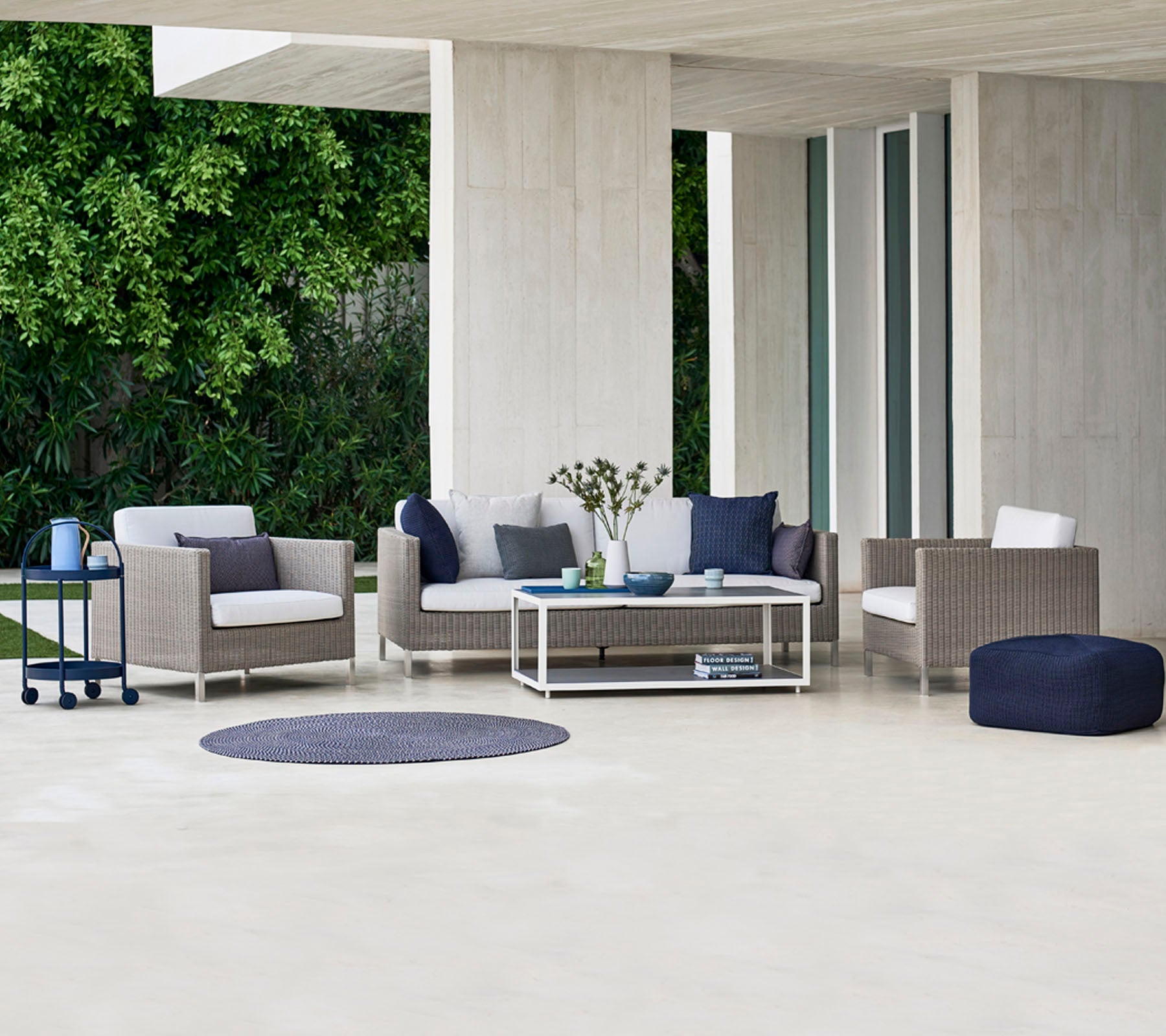 Zona de estar exterior contemporánea con un sofá, sillones y una mesa de café, complementada con cojines decorativos y una alfombra redonda.