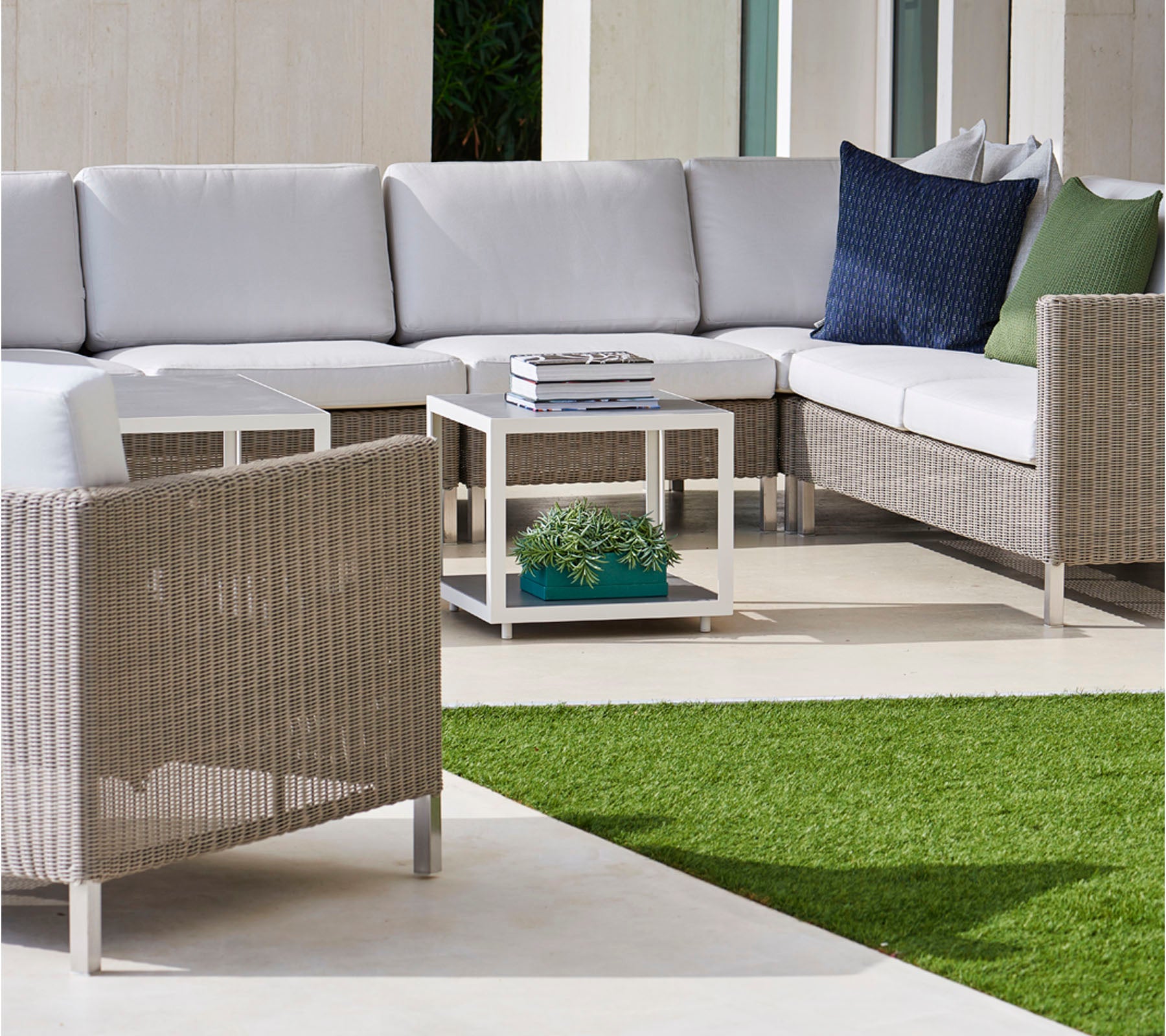 Área de estar exterior elegante con un sofá seccional con cojines grises, cojines acogedores y una mesa de café moderna sobre una superficie verde exuberante.