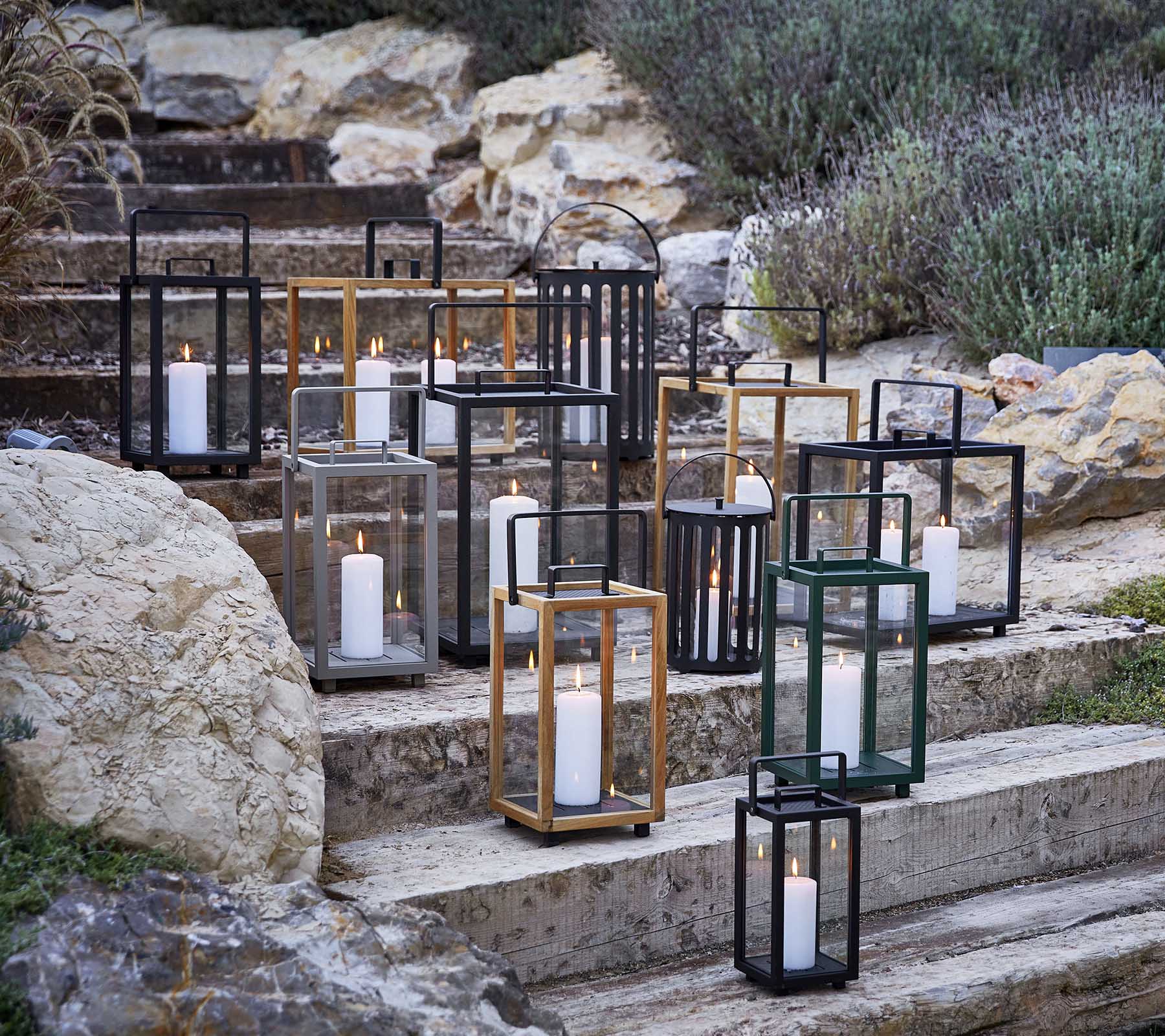 Colección de faroles decorativos en varios estilos y colores, con suave luz de vela, dispuestos artísticamente en escalones de piedra.