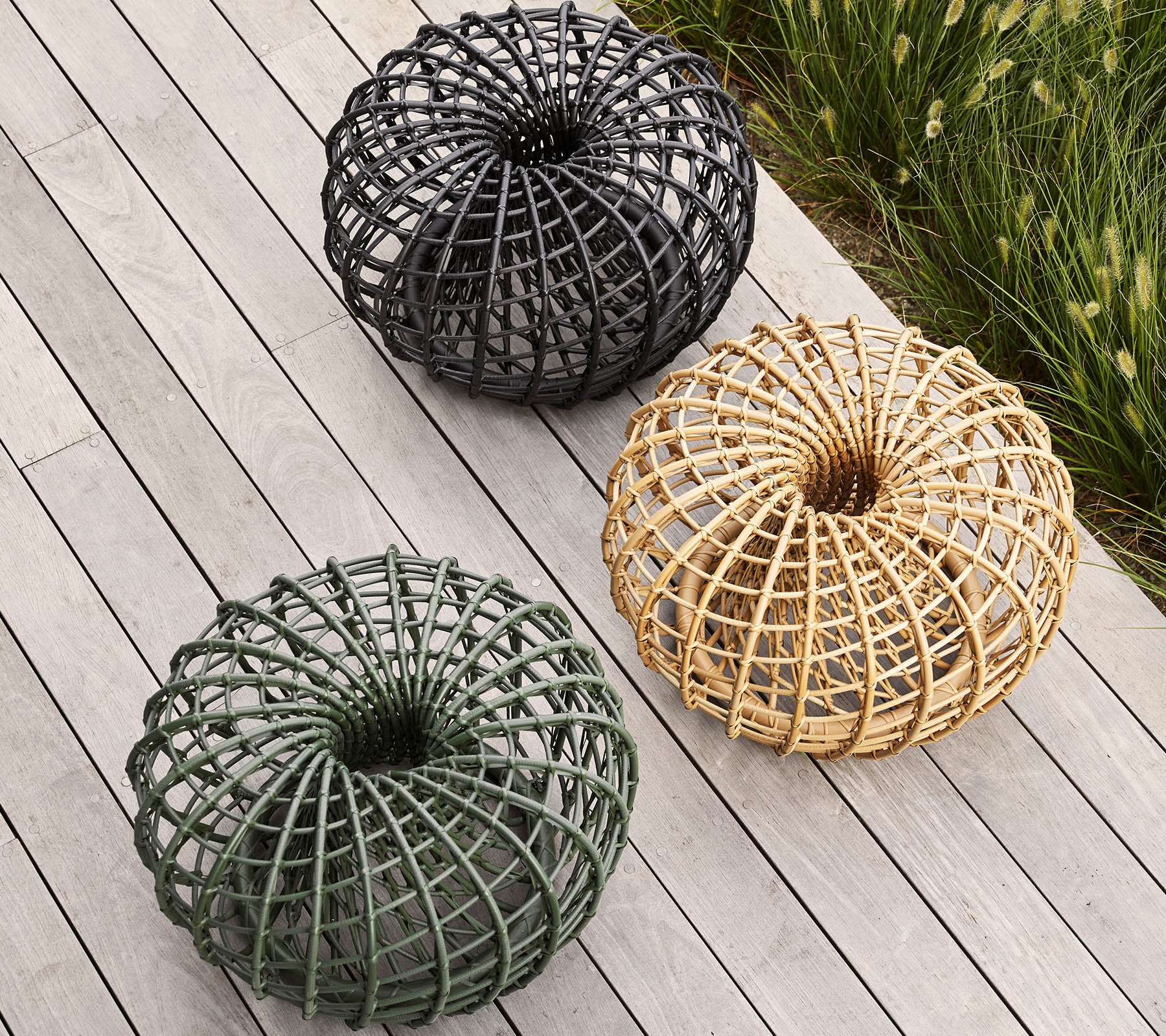 Tres cestas decorativas tejidas en negro, verde y tonos naturales, dispuestas en un patrón circular sobre una superficie de madera.