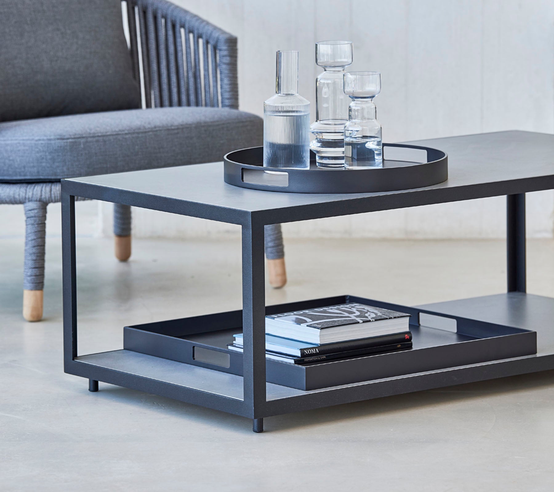 Mesa de café moderna con un diseño elegante, con una bandeja, vasos y libros en la estantería inferior. Ideal para espacios de vida con estilo.