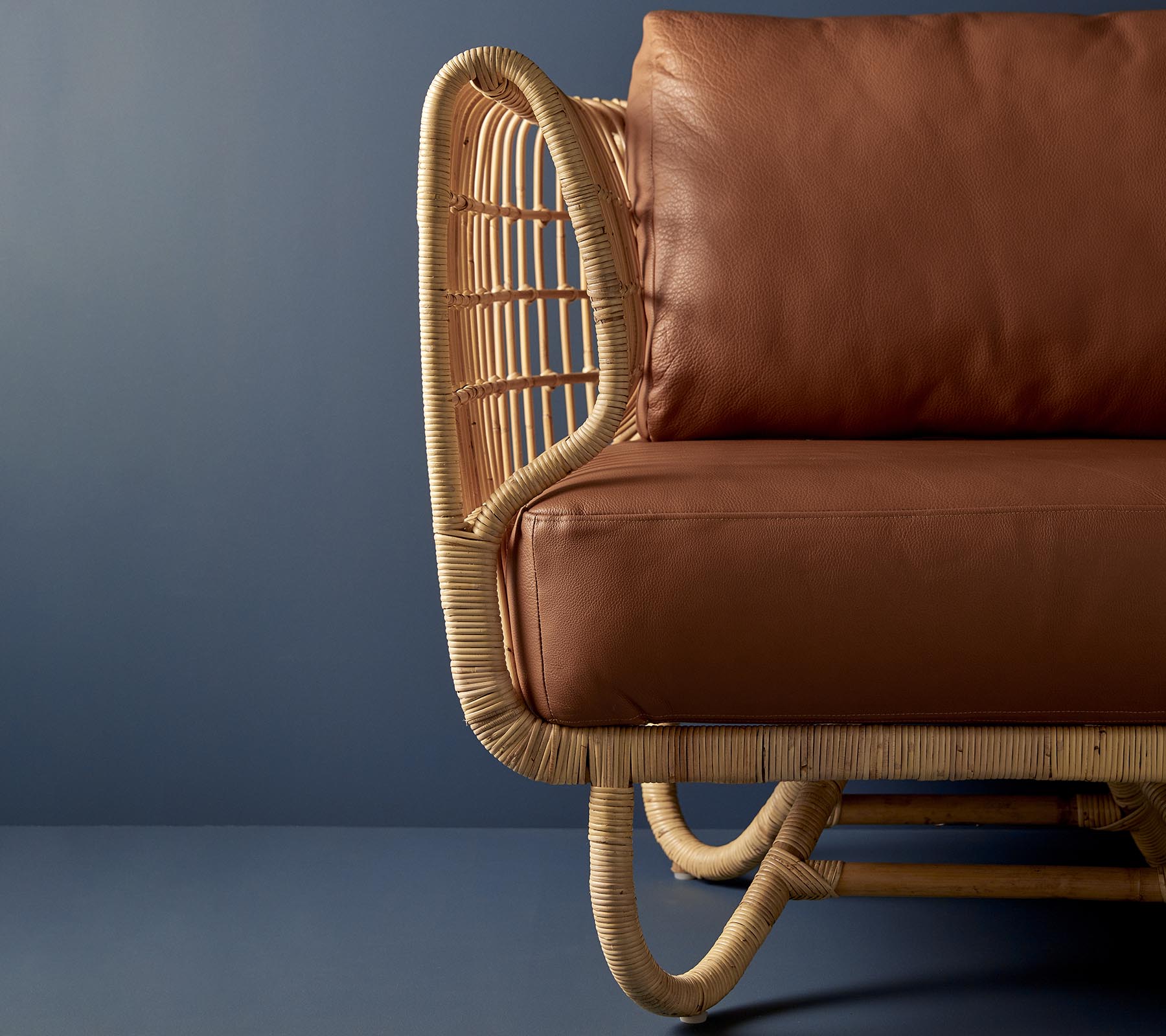 Silla de ratán con un diseño curvado y cojines de cuero marrón, que muestra una mezcla de materiales naturales y estética moderna.