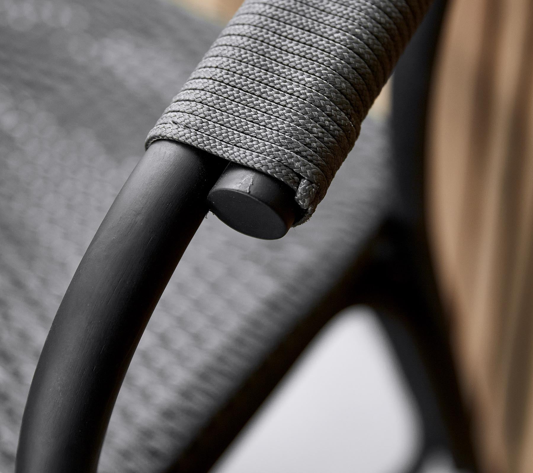 Close-up del reposabrazos de una silla elegante con un elegante marco negro y un revestimiento gris texturizado para un agarre cómodo.