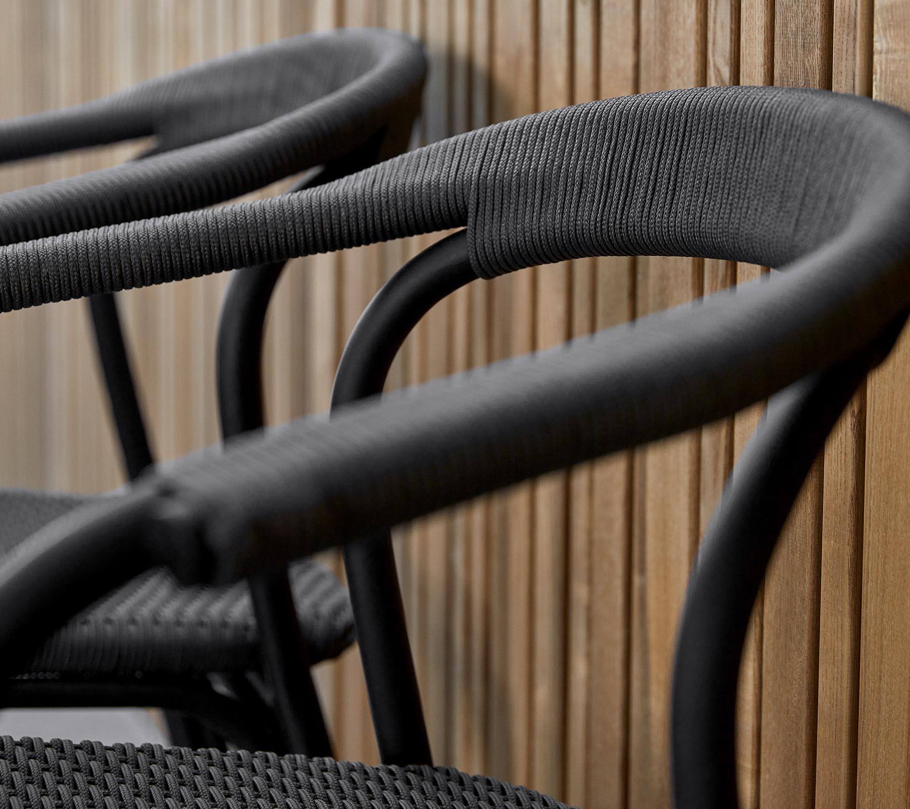 Tres sillas negras elegantes con brazos curvados, diseñadas con un acabado texturizado, contra un cálido fondo de madera.