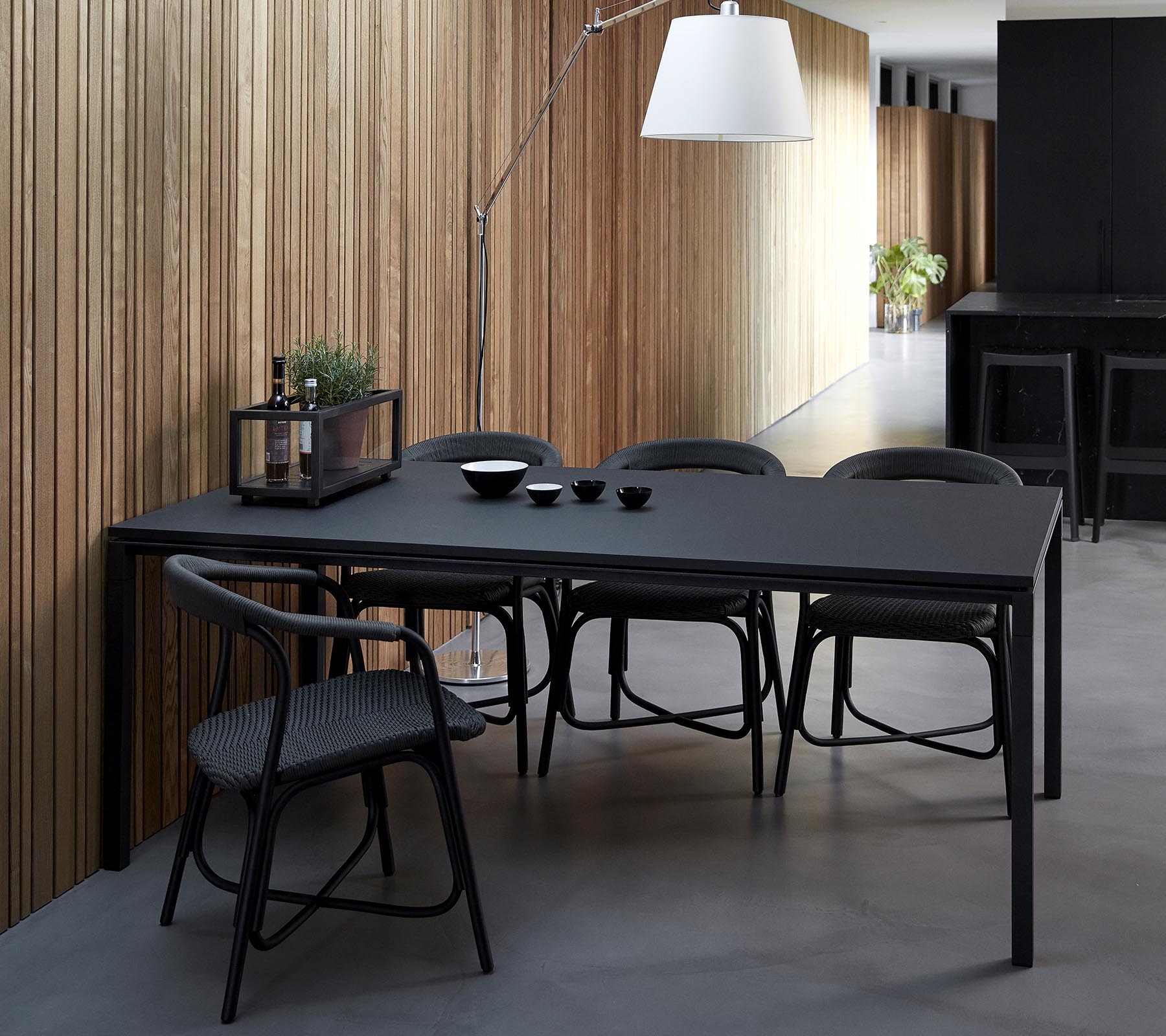 Una elegante mesa de comedor negra acompañada de sillas, decorada con cuencos y elementos decorativos, contra un fondo de paneles de madera.