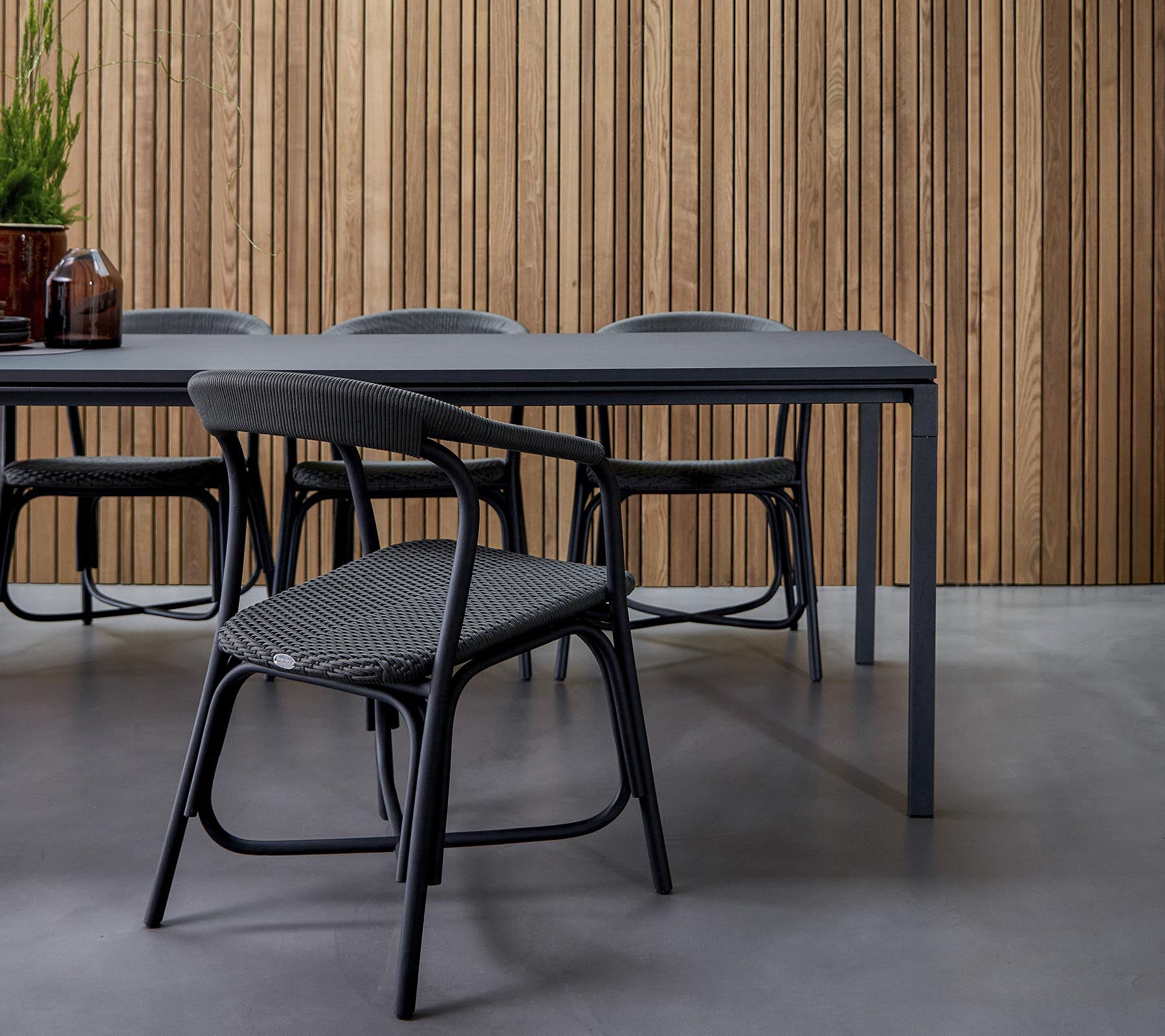 Un comedor moderno con una mesa elegante rodeada de sillas de diseño, contra un fondo de madera texturizada.