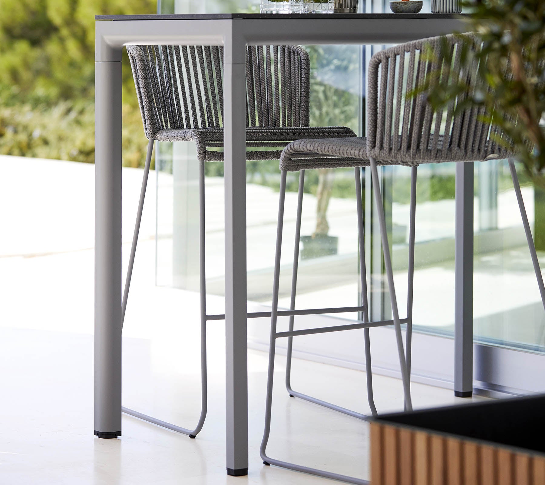 Una mesa elegante y moderna con taburetes altos a juego que presentan un diseño minimalista y un marco de metal estilizado, complementada con vegetación natural.