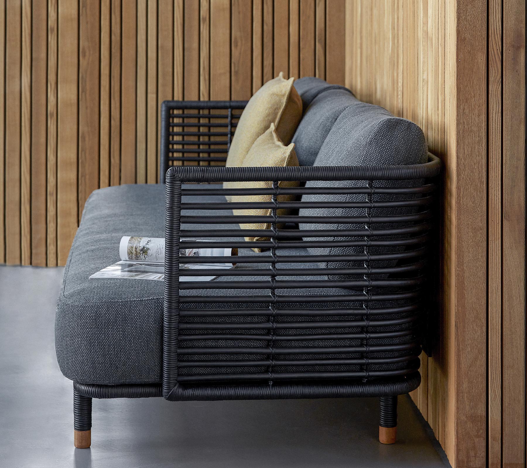 Sofá elegante con un diseño estilizado en tejido gris texturizado y cojines decorativos, complementado por un moderno marco de lamas.