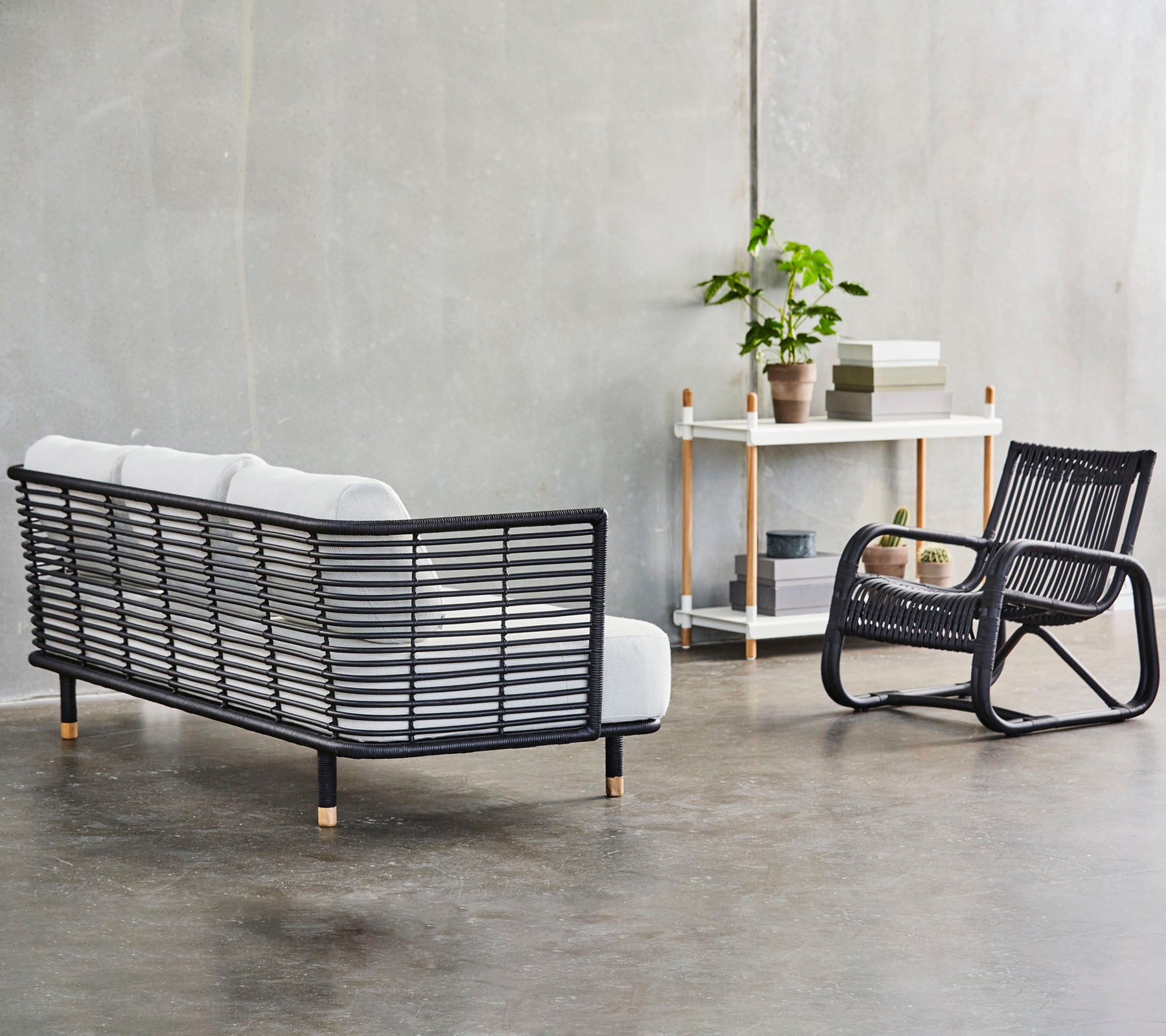 Un arreglo de asientos moderno con un sofá de marco negro elegante con cojines blancos y un sillón mecedor a juego, acentuado por vegetación.