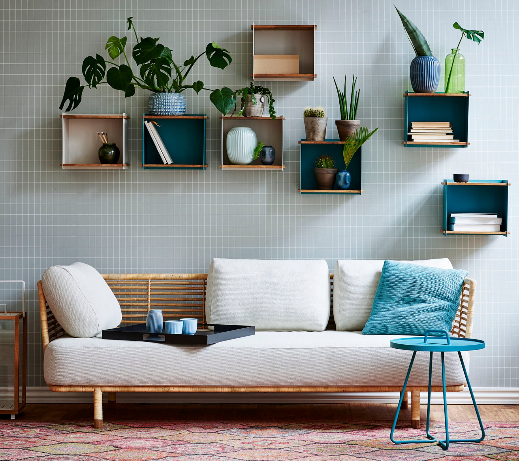 Un sofá elegante con un cojín ligero y una mesa pequeña, adornado con varias plantas en maceta expuestas en estanterías geométricas.