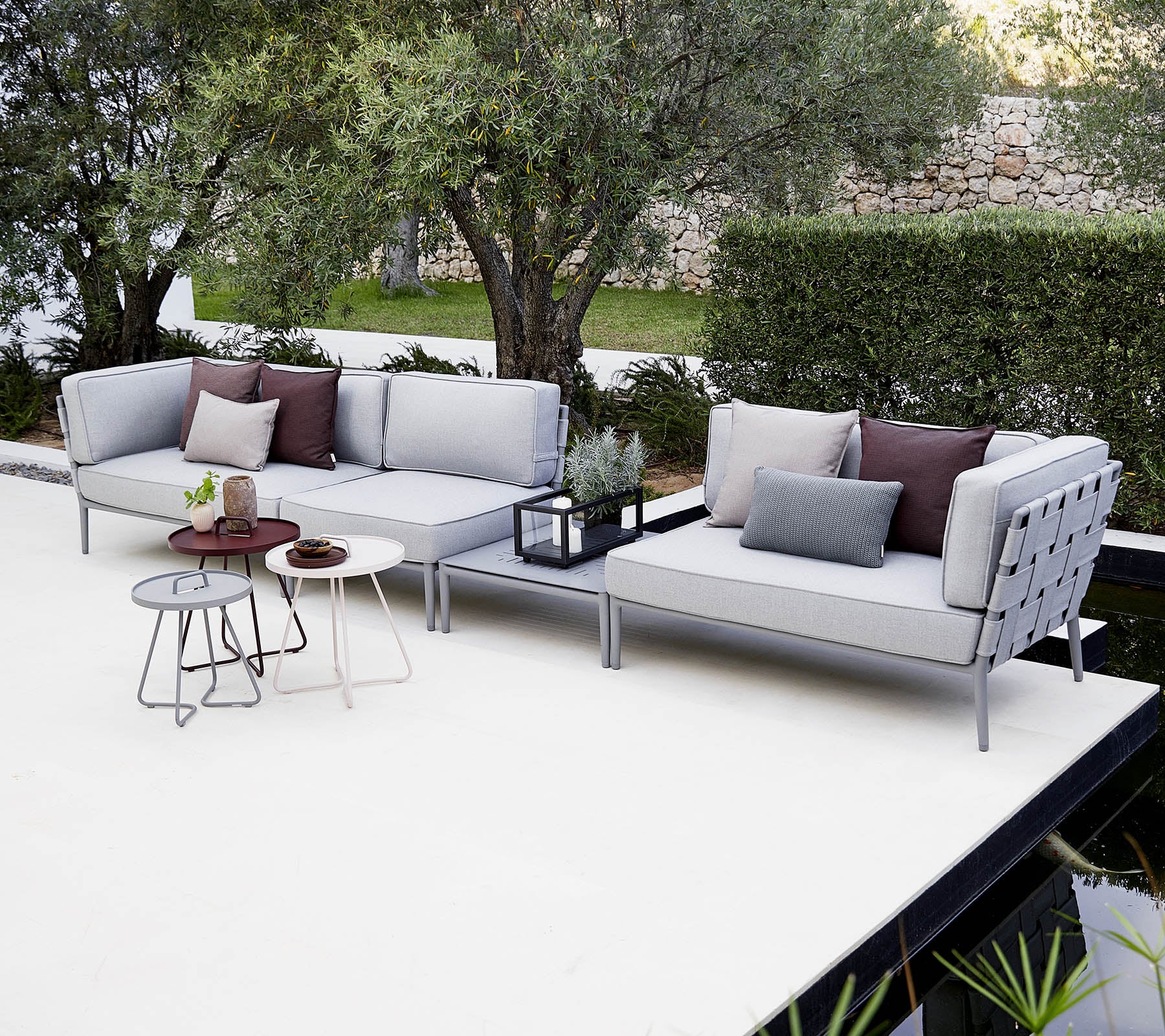 Conjunto moderno de asientos al aire libre con cojines, acompañado de una mesa auxiliar elegante y plantas decorativas.