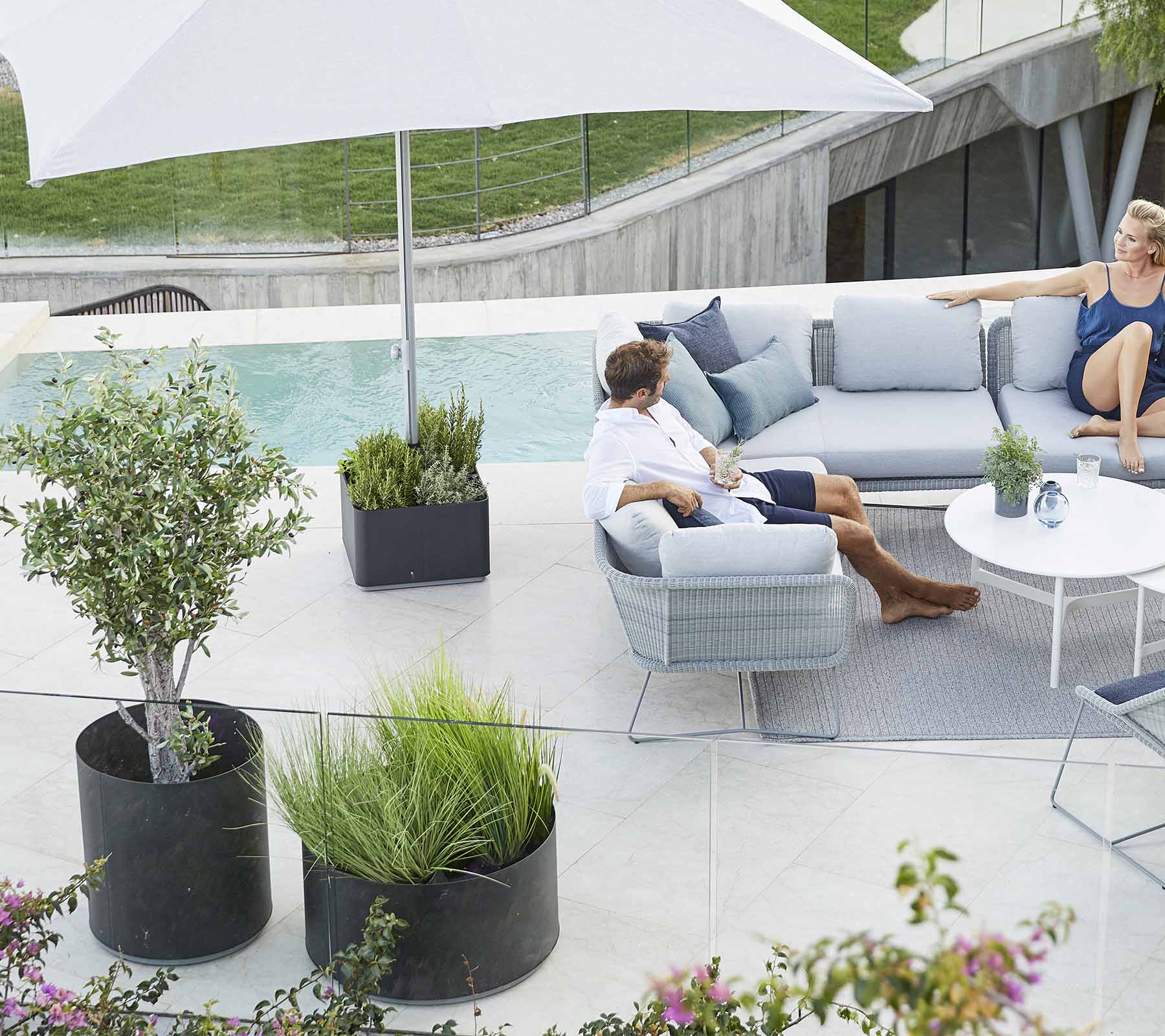 Un área de estar al aire libre elegante con un sofá cómodo, plantas y un gran paraguas, perfecta para relajarse.