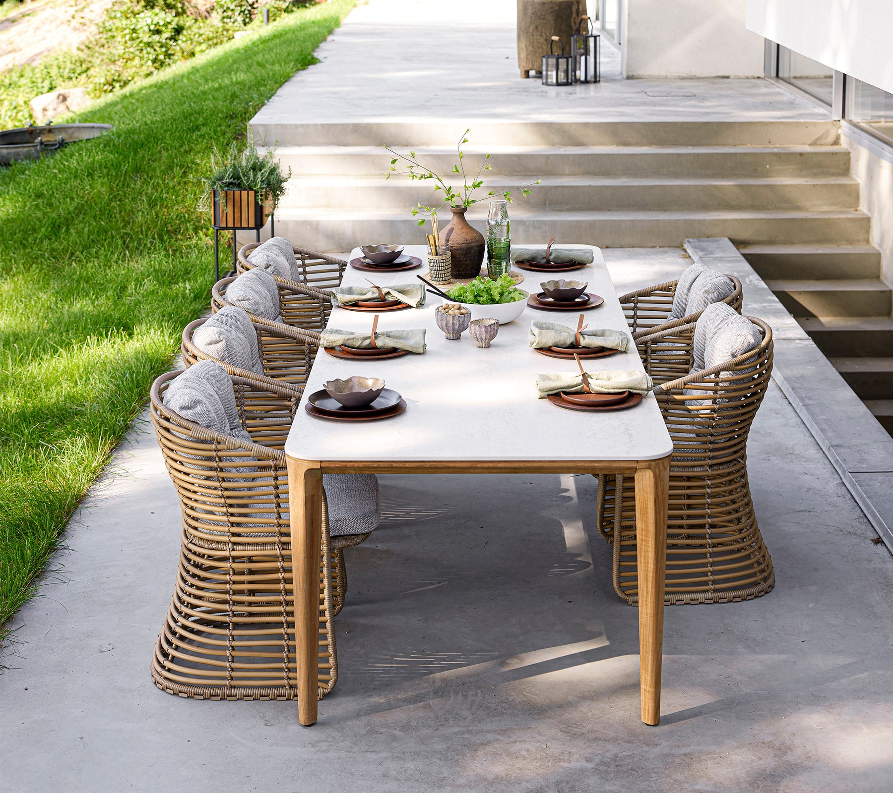 Un juego de comedor elegante con vajilla elegante y cómodas sillas, rodeado de vegetación y luz natural. Perfecto para reuniones.