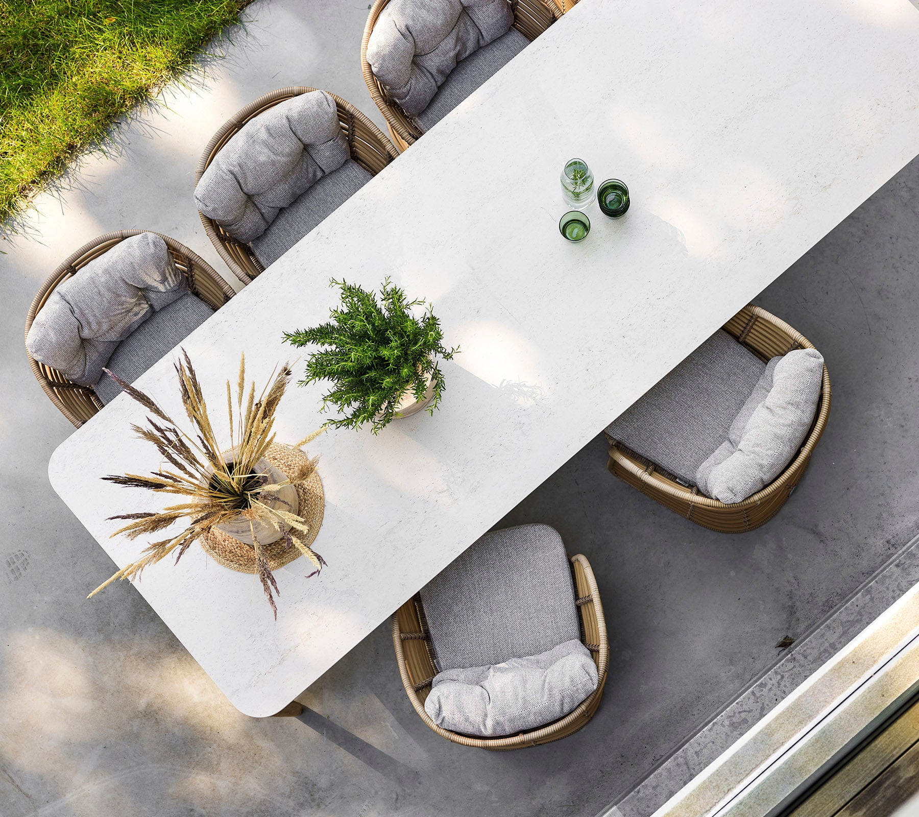 Una mesa rectangular elegante rodeada de cuatro sillas cómodas, adornada con vegetación y elementos decorativos en la parte superior.