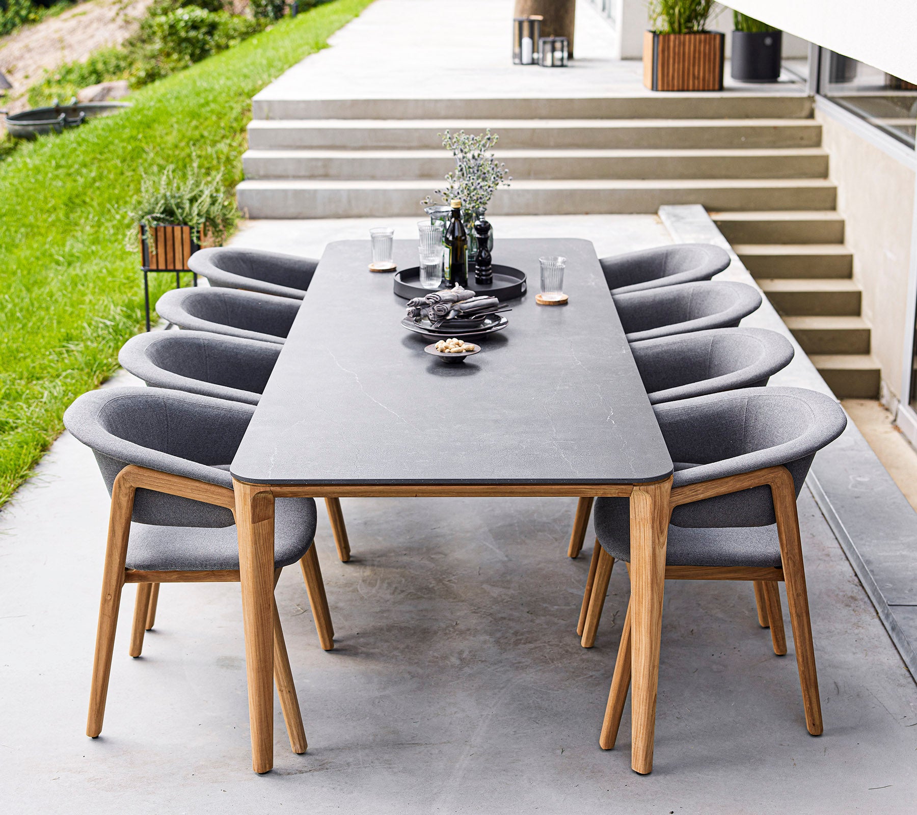 Una mesa de comedor moderna con ocho sillas grises, que presenta elementos decorativos y plantas en la mesa, ubicada en un elegante espacio al aire libre.